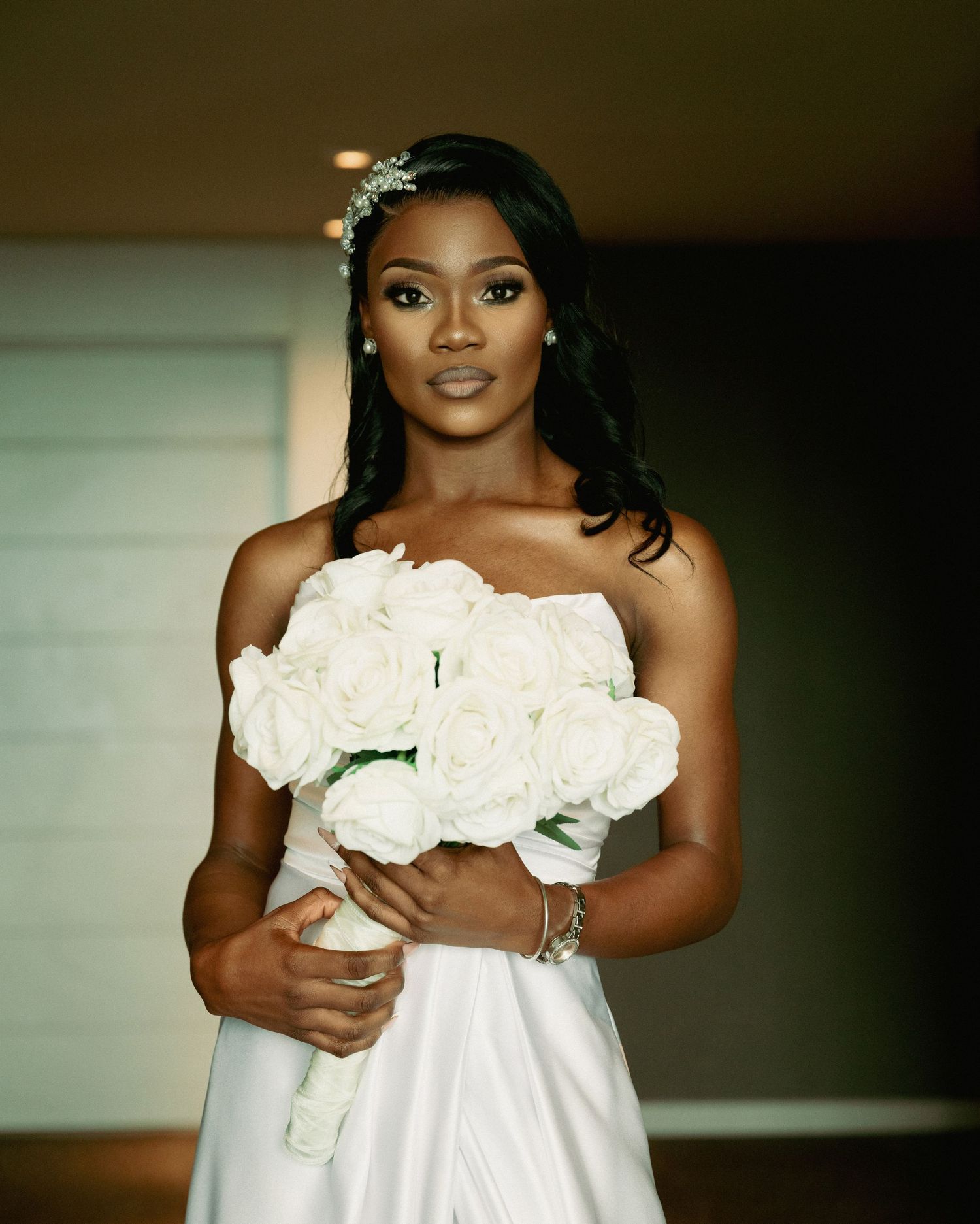 Elegant bride in strapless white gown holding white rose bouquet with floral hair accessory.