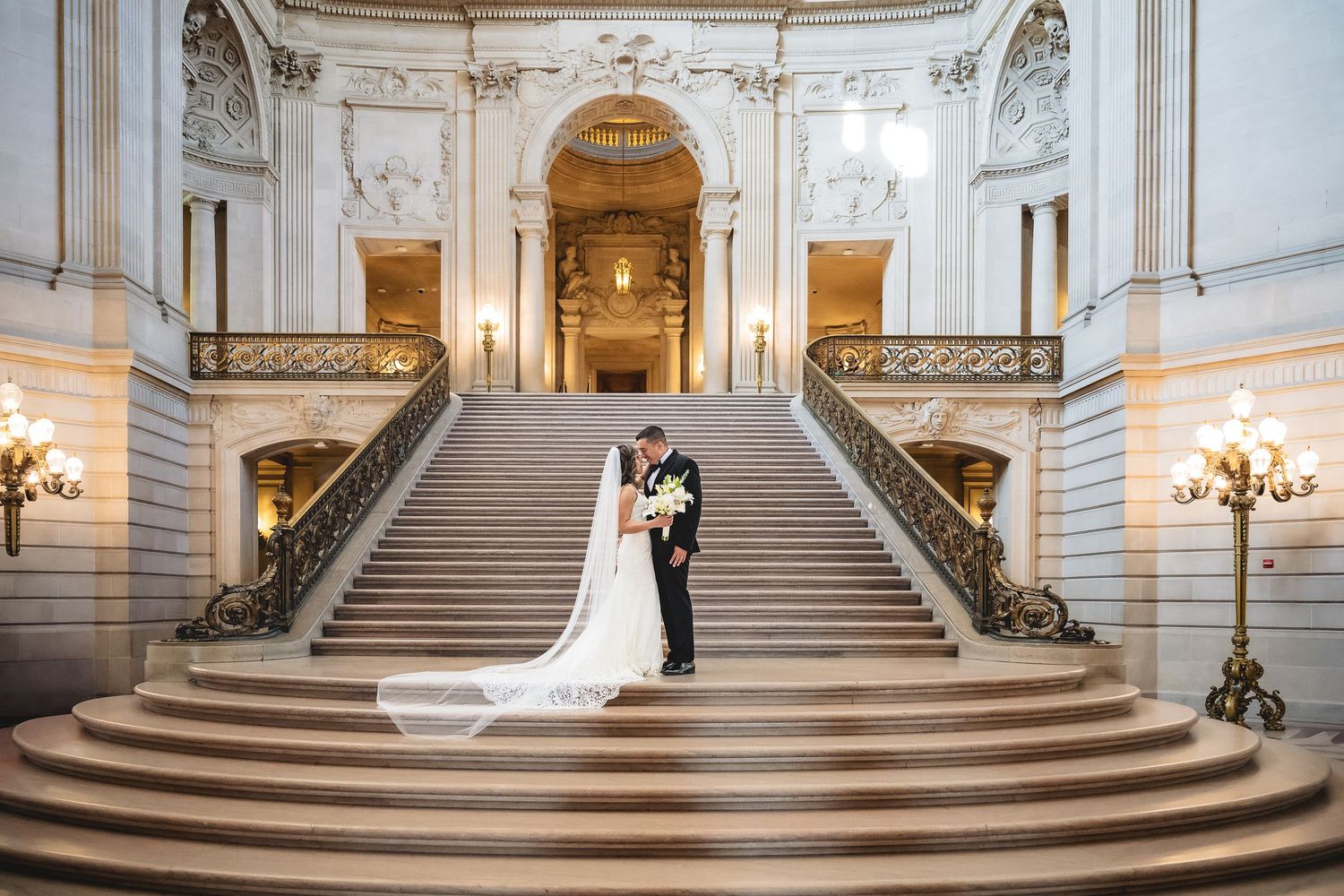 Bride and groom share a romantic kiss on the grand staircase of San Francisco City Hall on their wedding day.