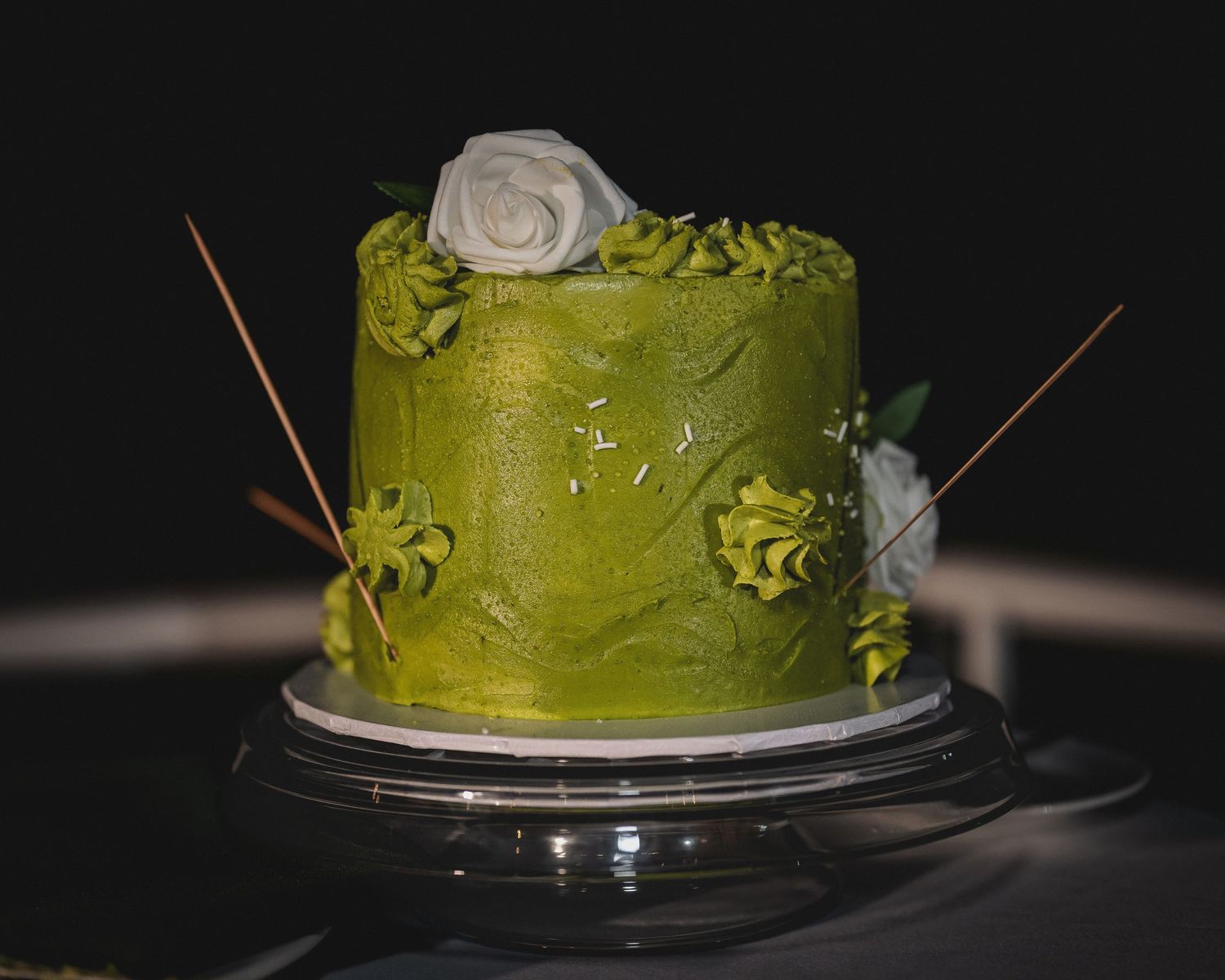 Elegant green frosted cake with white rose and gold accents on a dark background.