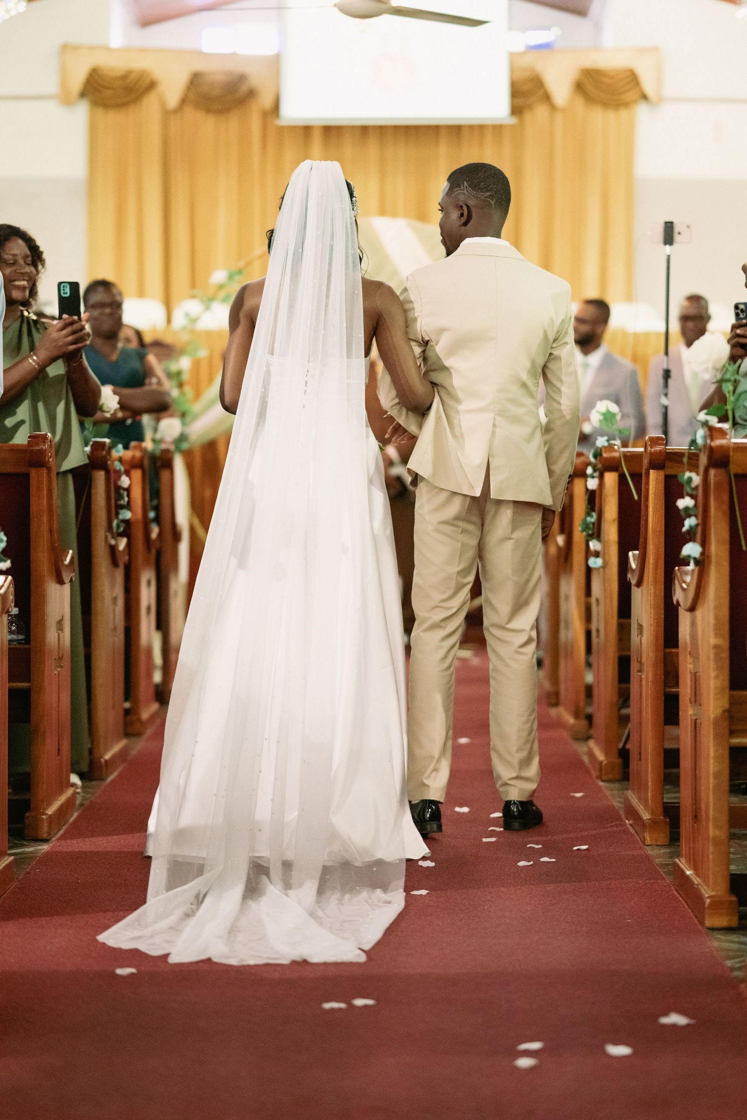 Bride and groom walking down church aisle after wedding ceremony, bride wearing white gown and veil.