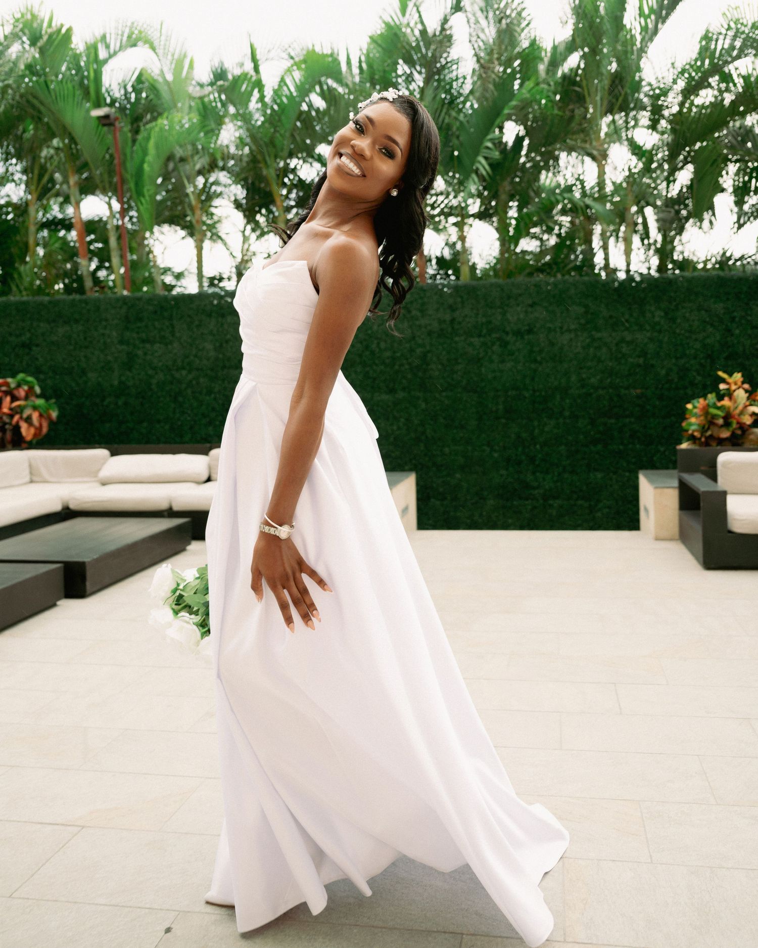 Radiant bride twirls in elegant white strapless wedding gown on outdoor patio surrounded by tropical greenery.