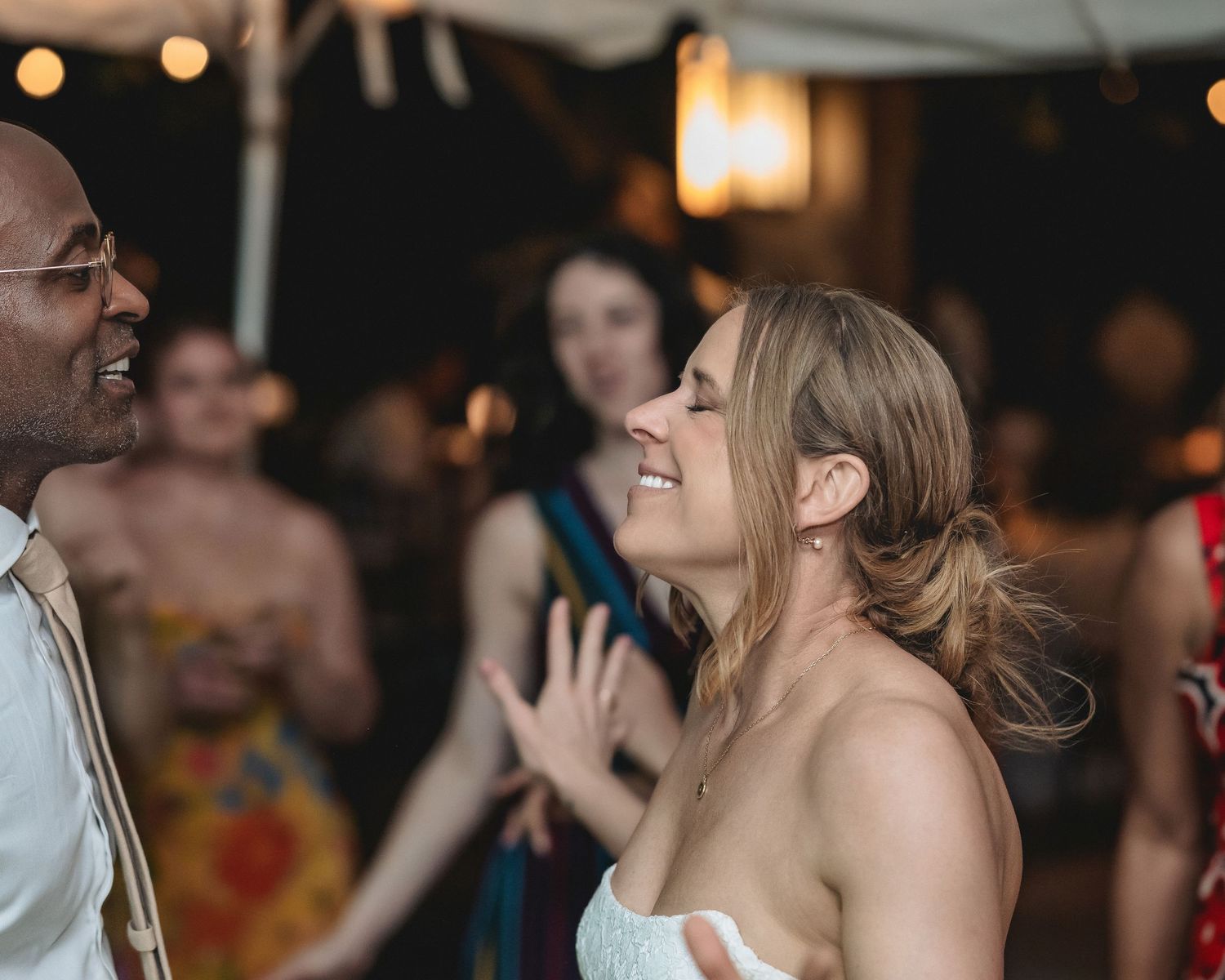 Bride and groom share a joyful dance moment at an outdoor wedding reception with guests celebrating in the background.
