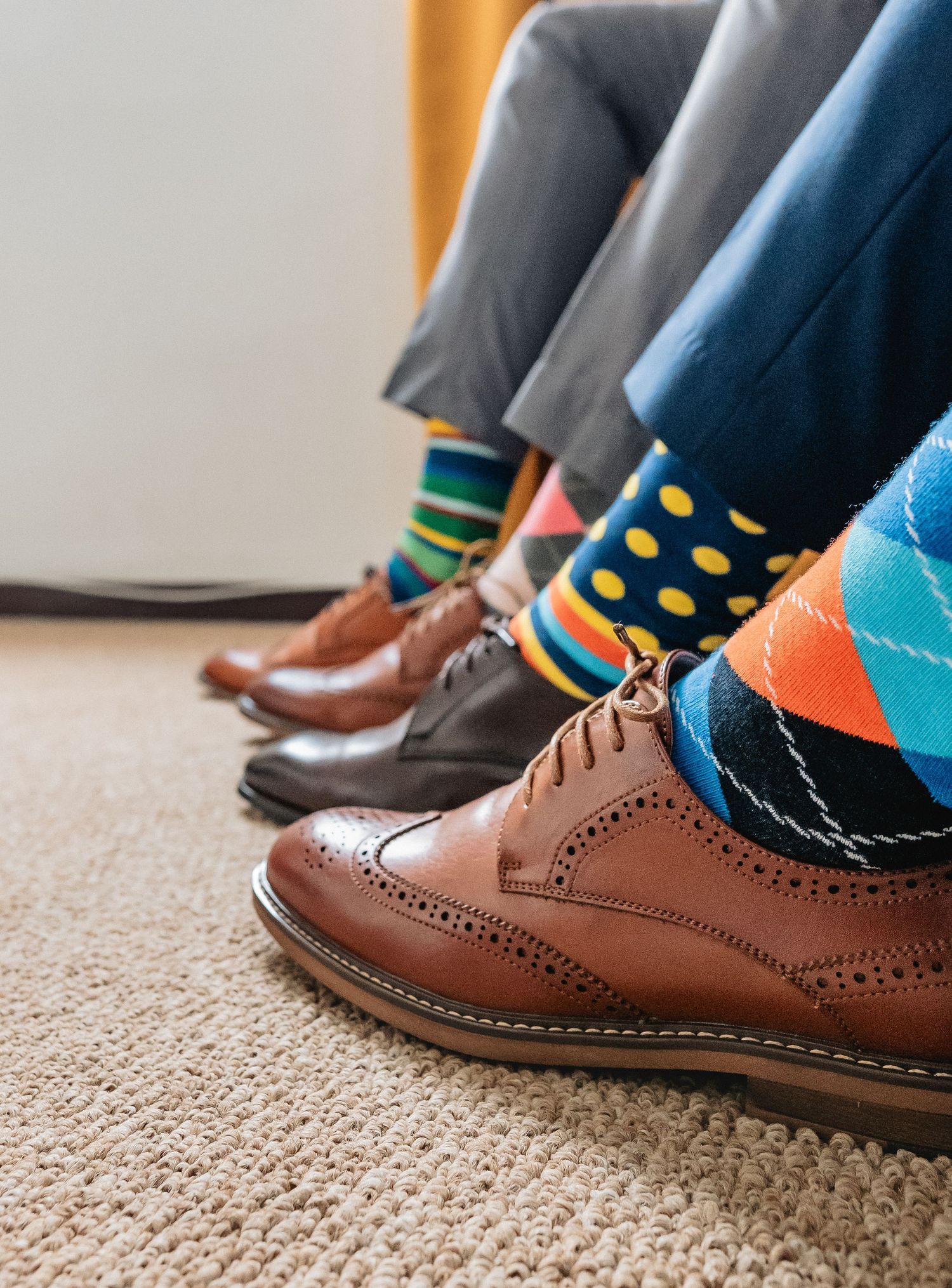 Close-up of three men wearing colorful patterned socks with brown brogue dress shoes at a wedding.