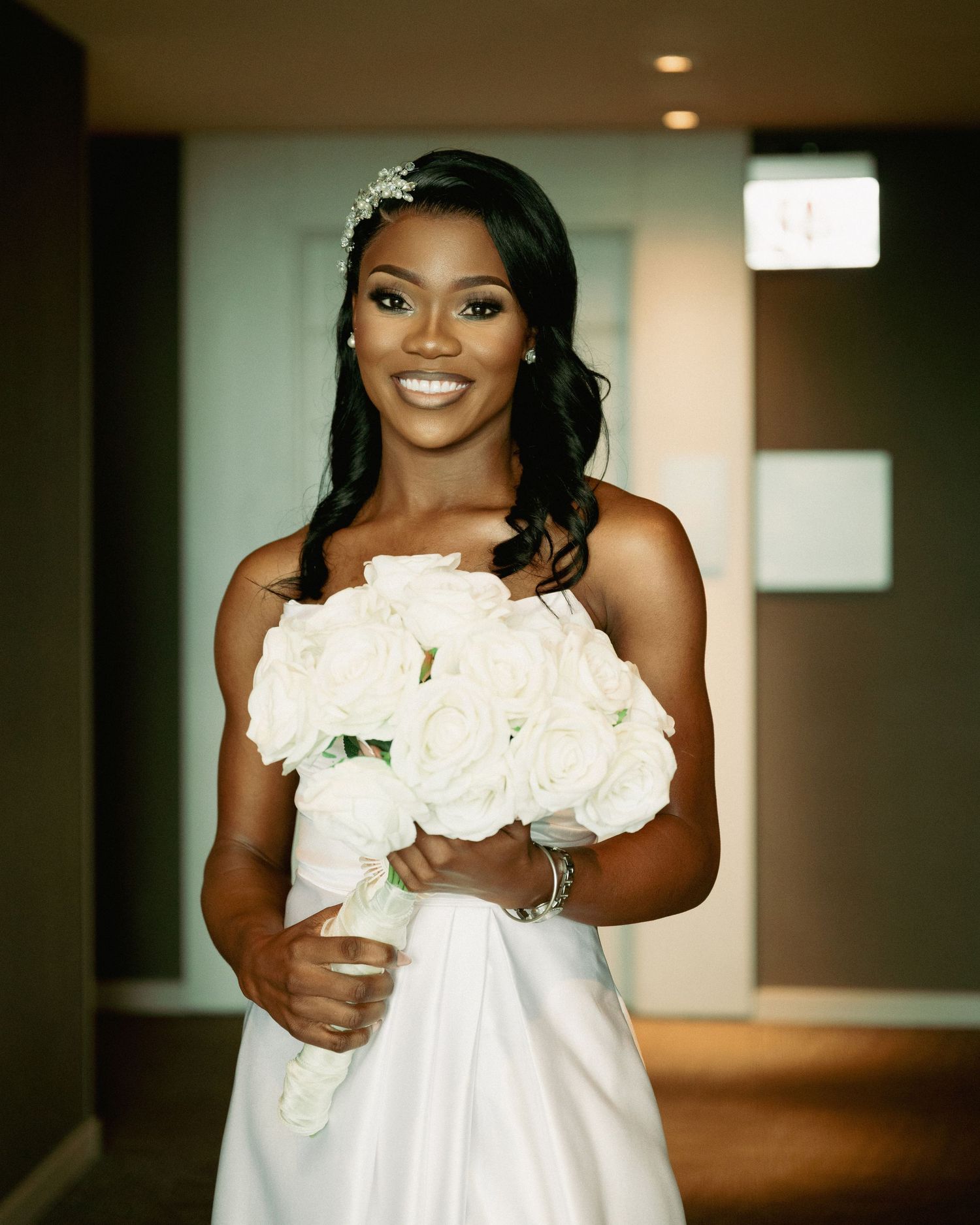 Bride holds white rose bouquet while posing in elegant indoor setting.
