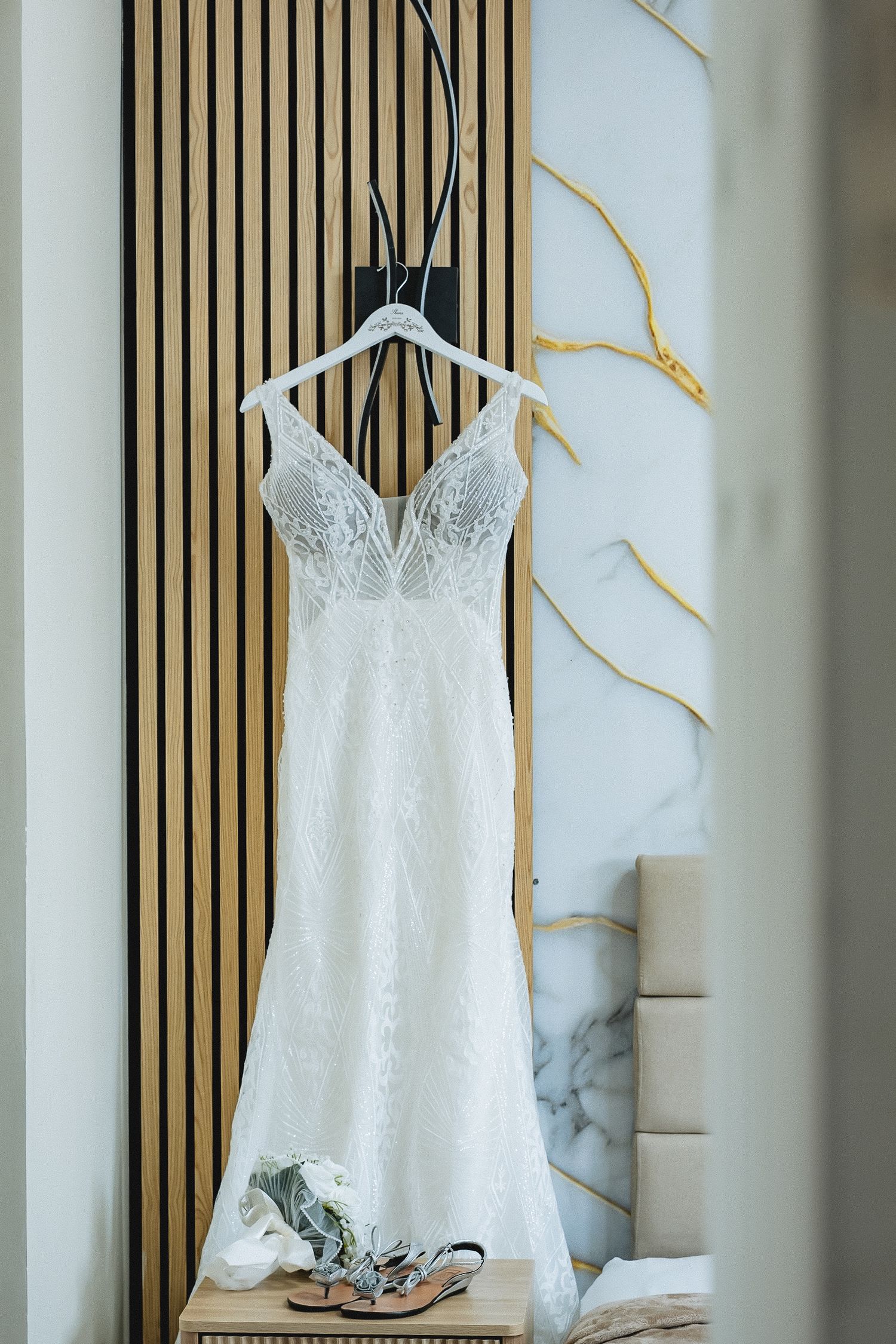 A white lace wedding dress hangs on display against a modern wooden slatted wall.