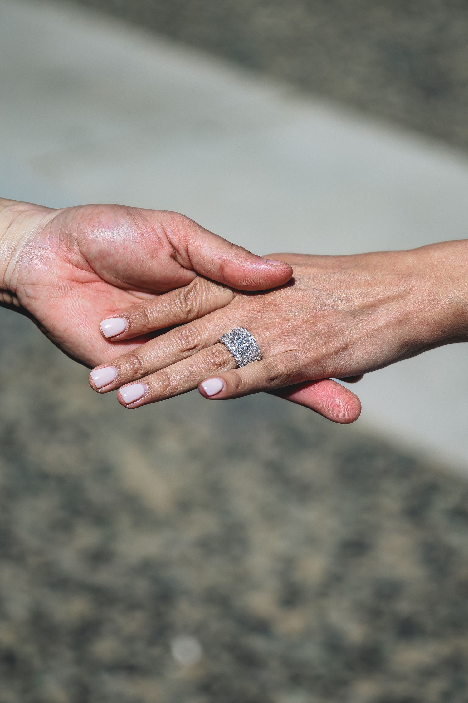 Two hands gently touching, one wearing a sparkling diamond ring with white manicured nails, symbolizing love and commitment.