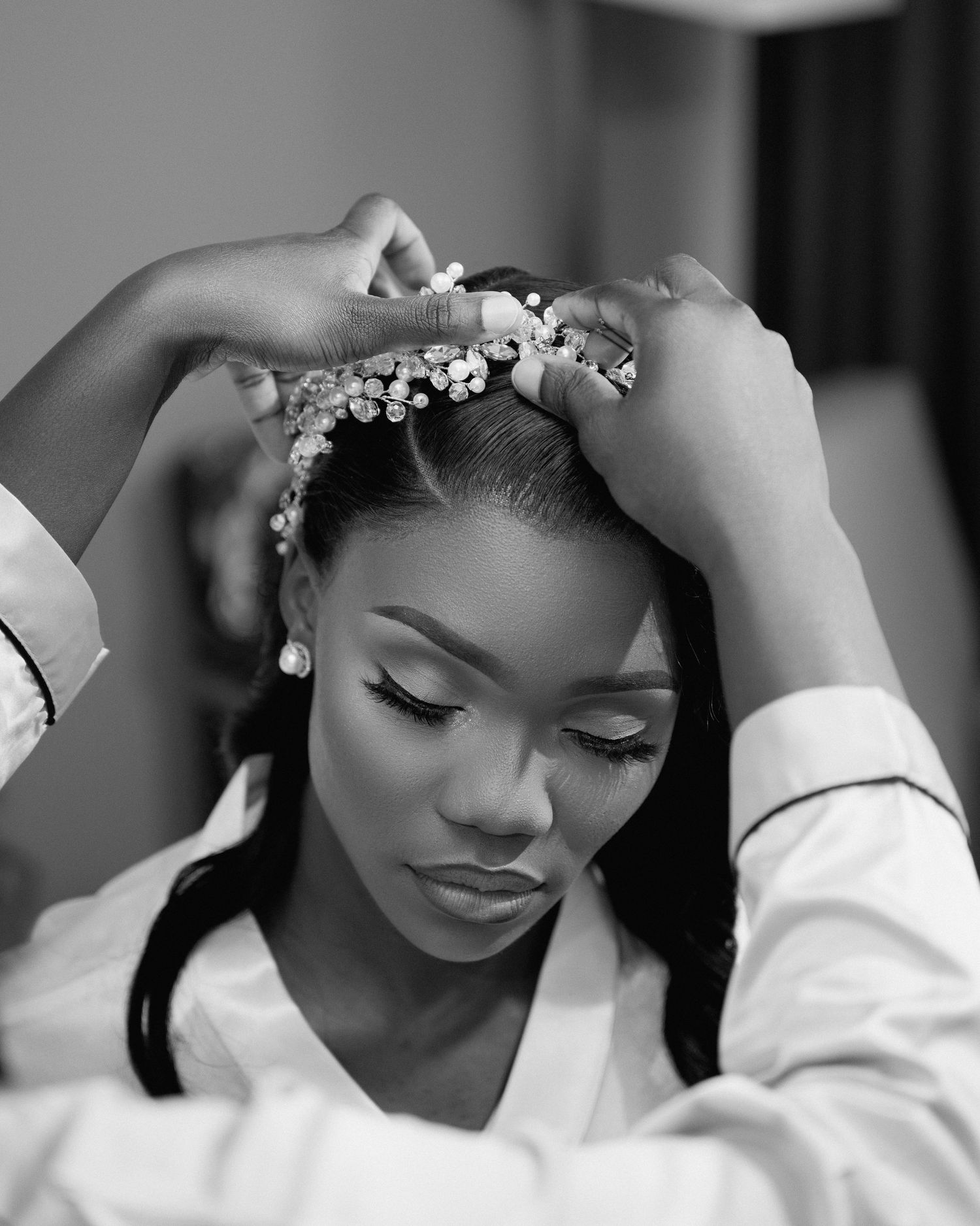 Black and white photo of bride having crystal tiara placed on her hair during wedding preparations.