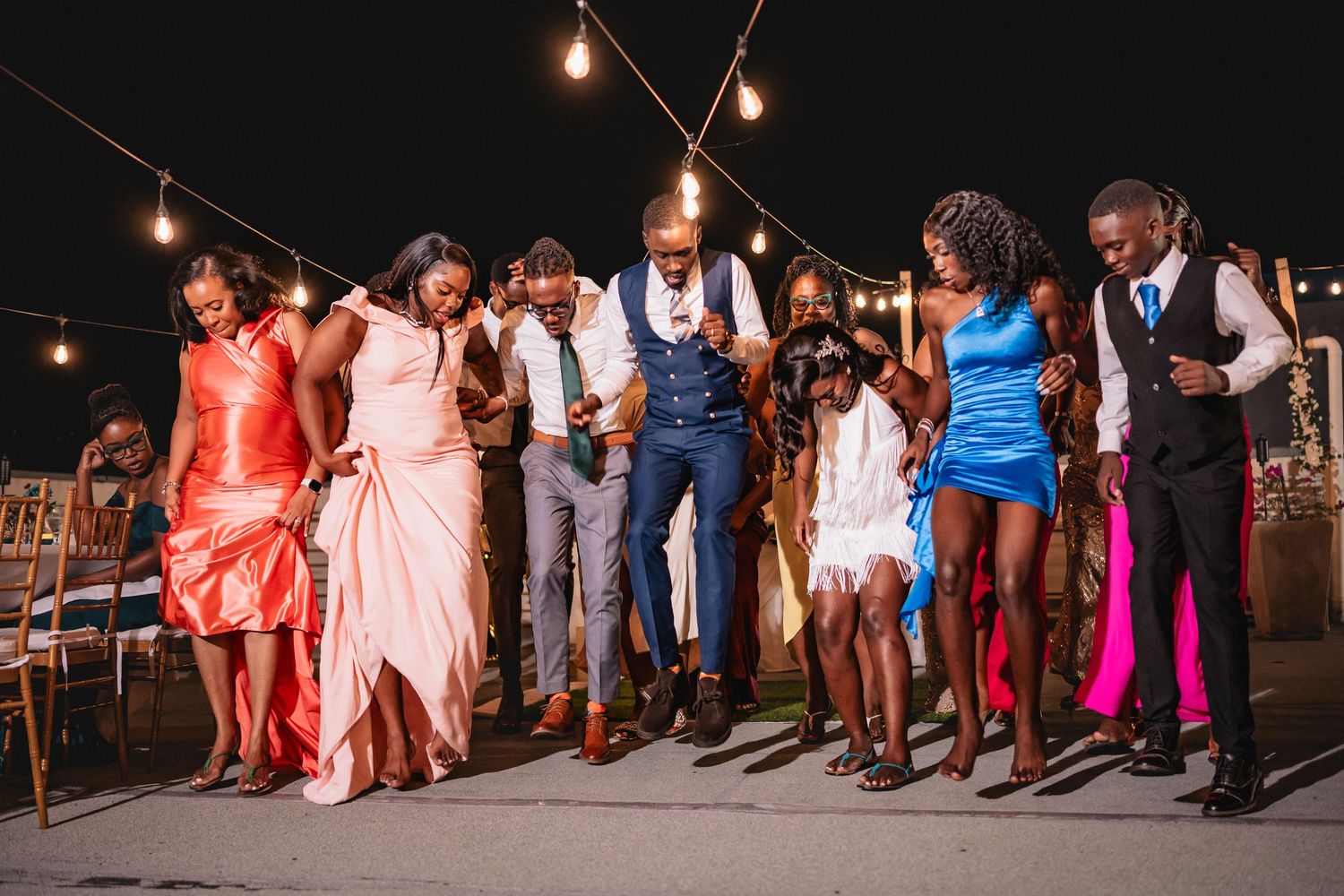 Wedding guests dancing joyfully outdoors at night under warm string lights.
