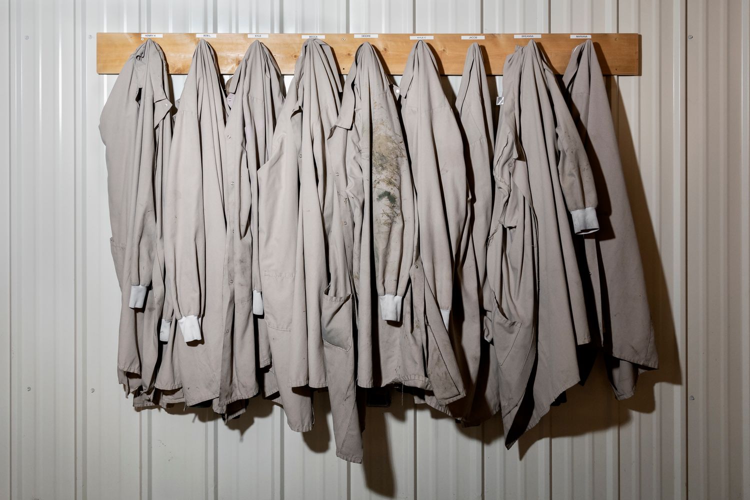 Row of gray lab coats hanging on hooks against white wall.