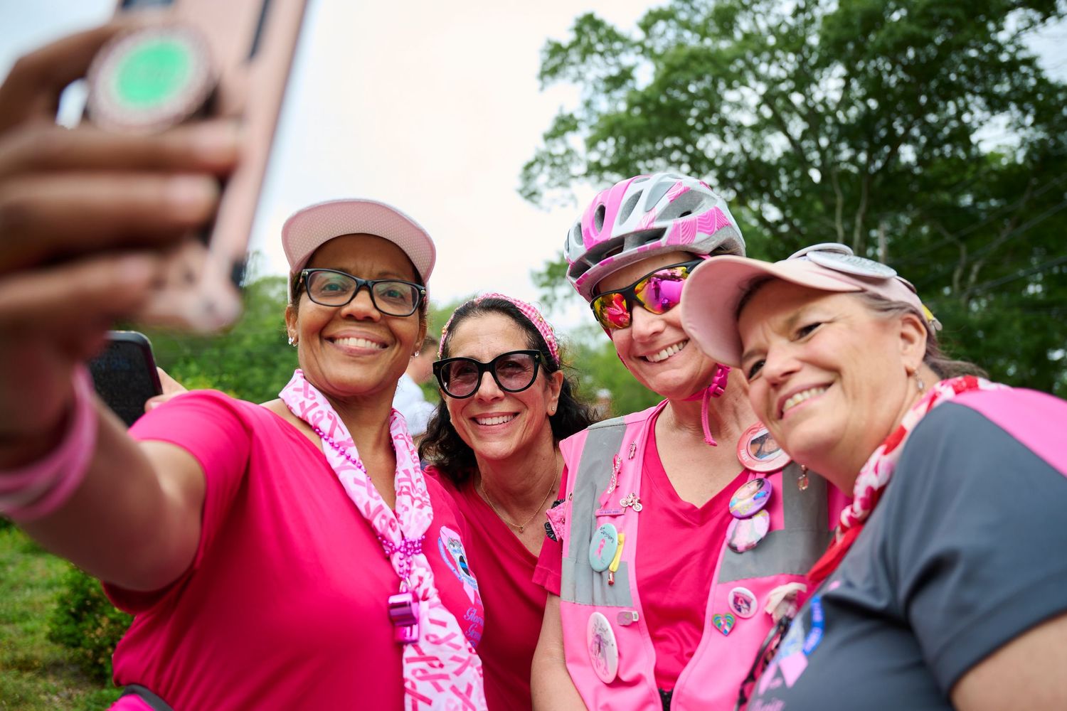 Four women in pink outfits take a selfie outdoors during a breast cancer awareness charity walk event.
