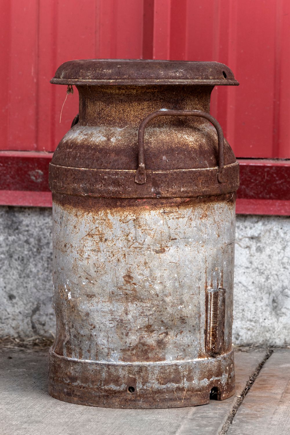 Rustic metal milk can with weathered patina against a red and grey background.