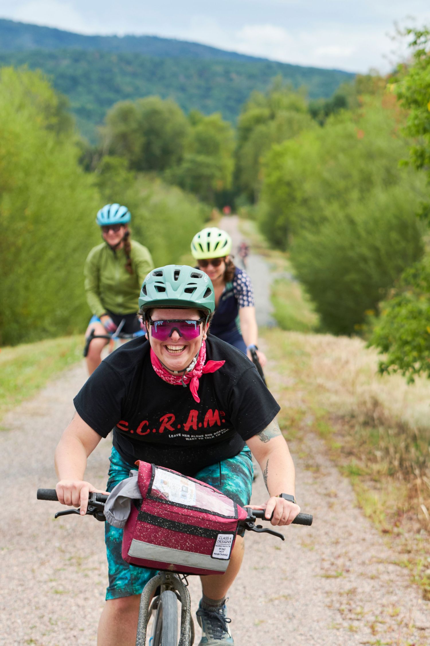 Mountain biker in colorful gear riding on a gravel trail with rolling hills in the background.