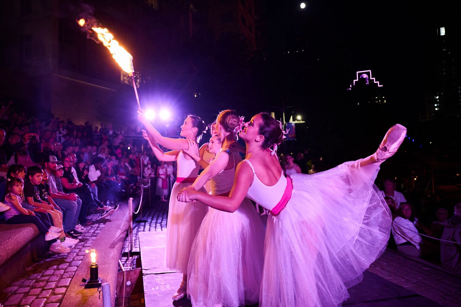 Dancers in flowing white dresses perform on a dimly lit stage with dramatic purple lighting effects.