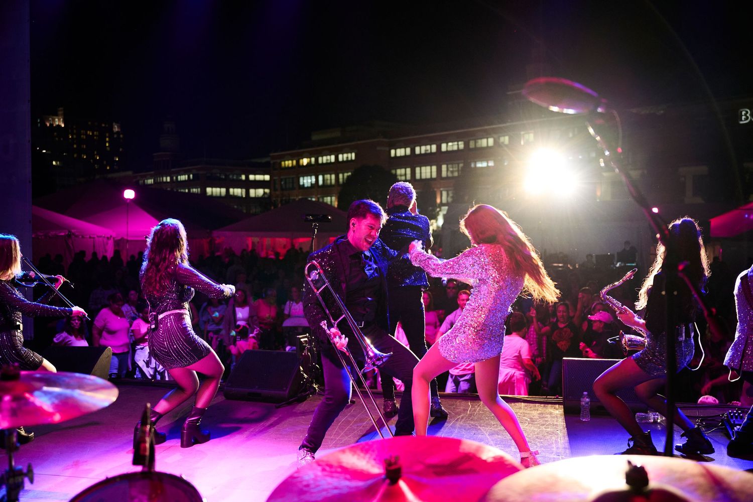 Performers dance energetically on a pink-lit stage during a nighttime show.
