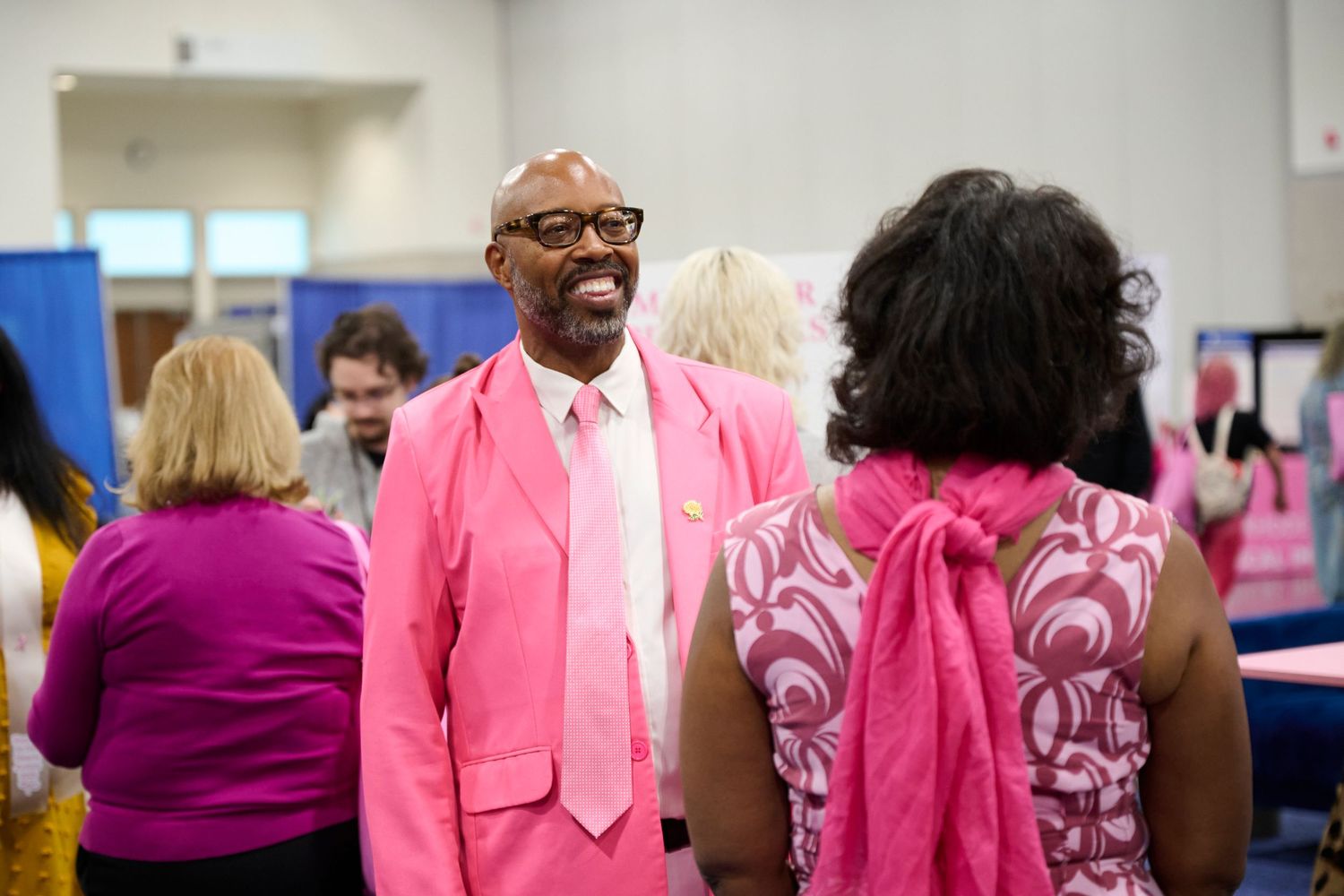 People wearing pink outfits and formal attire gather at an indoor event supporting breast cancer awareness.