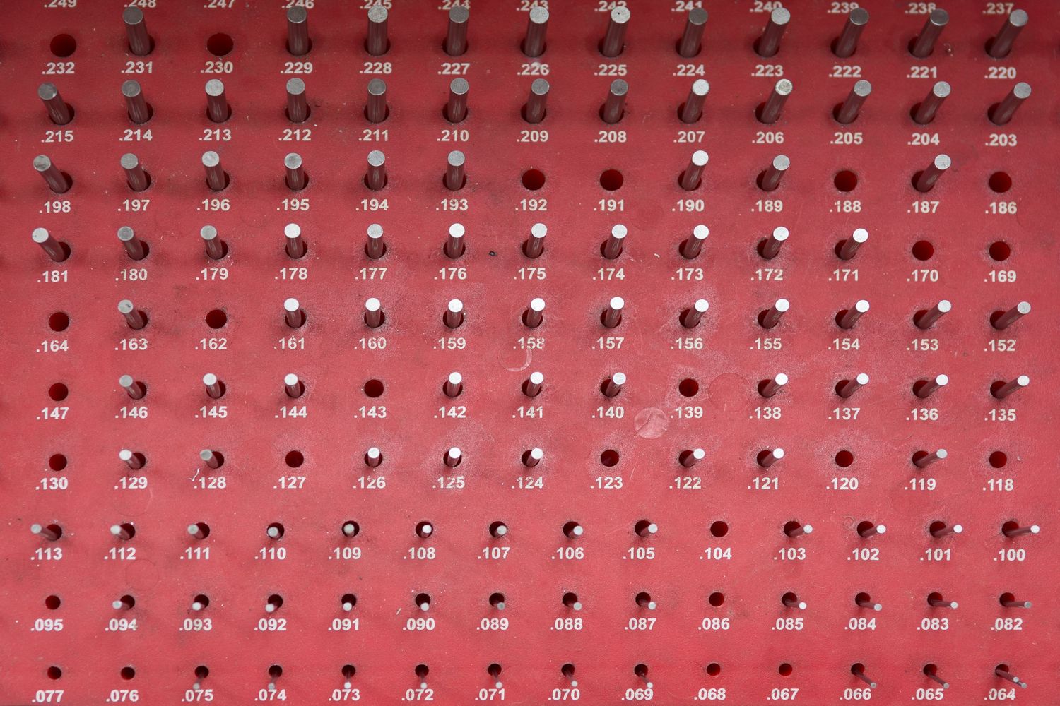 Red wall display with rows of identical small circular objects arranged in a grid pattern.