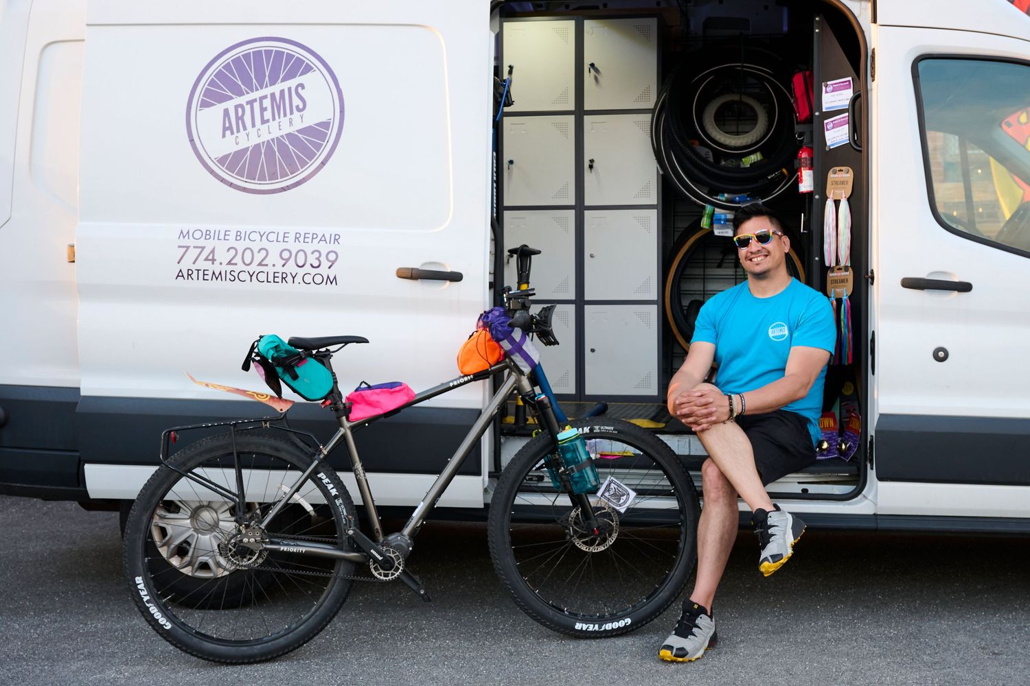 Man sitting in van door beside loaded touring bike at Artemis Mobile Bicycle Repair shop.