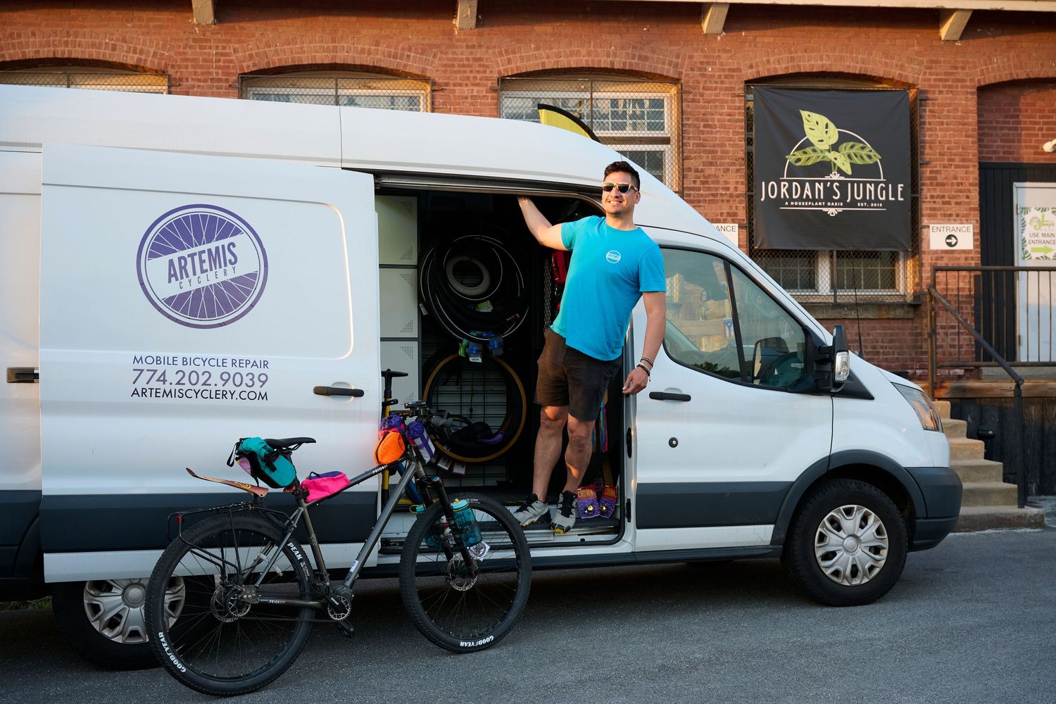 Delivery vans and cargo bikes parked outside a brick building with loading docks for urban logistics operations.