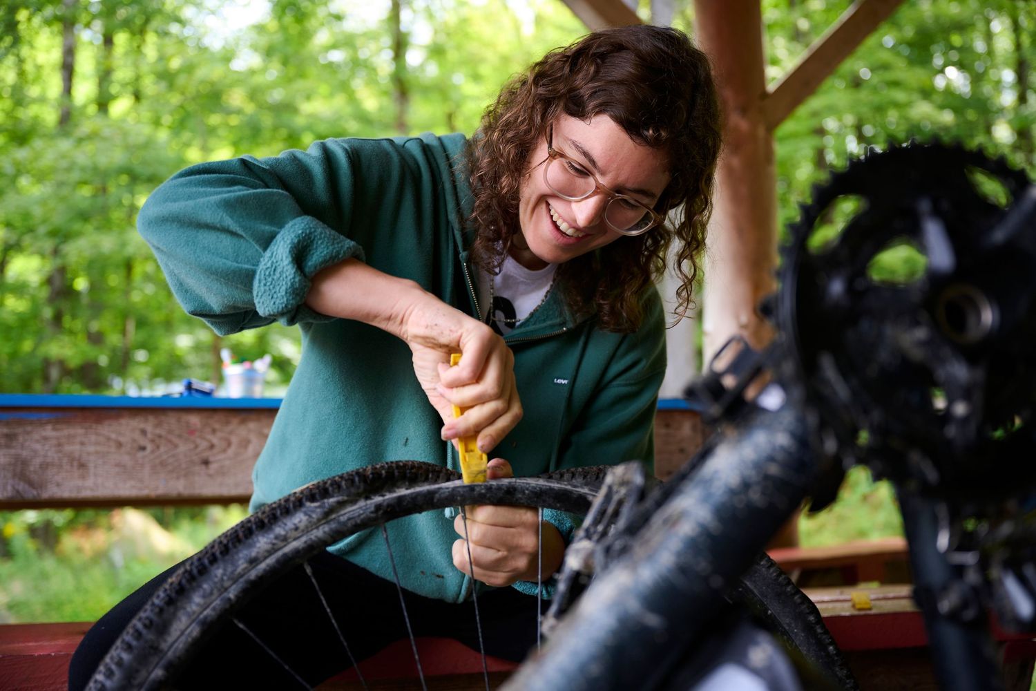Person working on bicycle maintenance under an outdoor shelter.