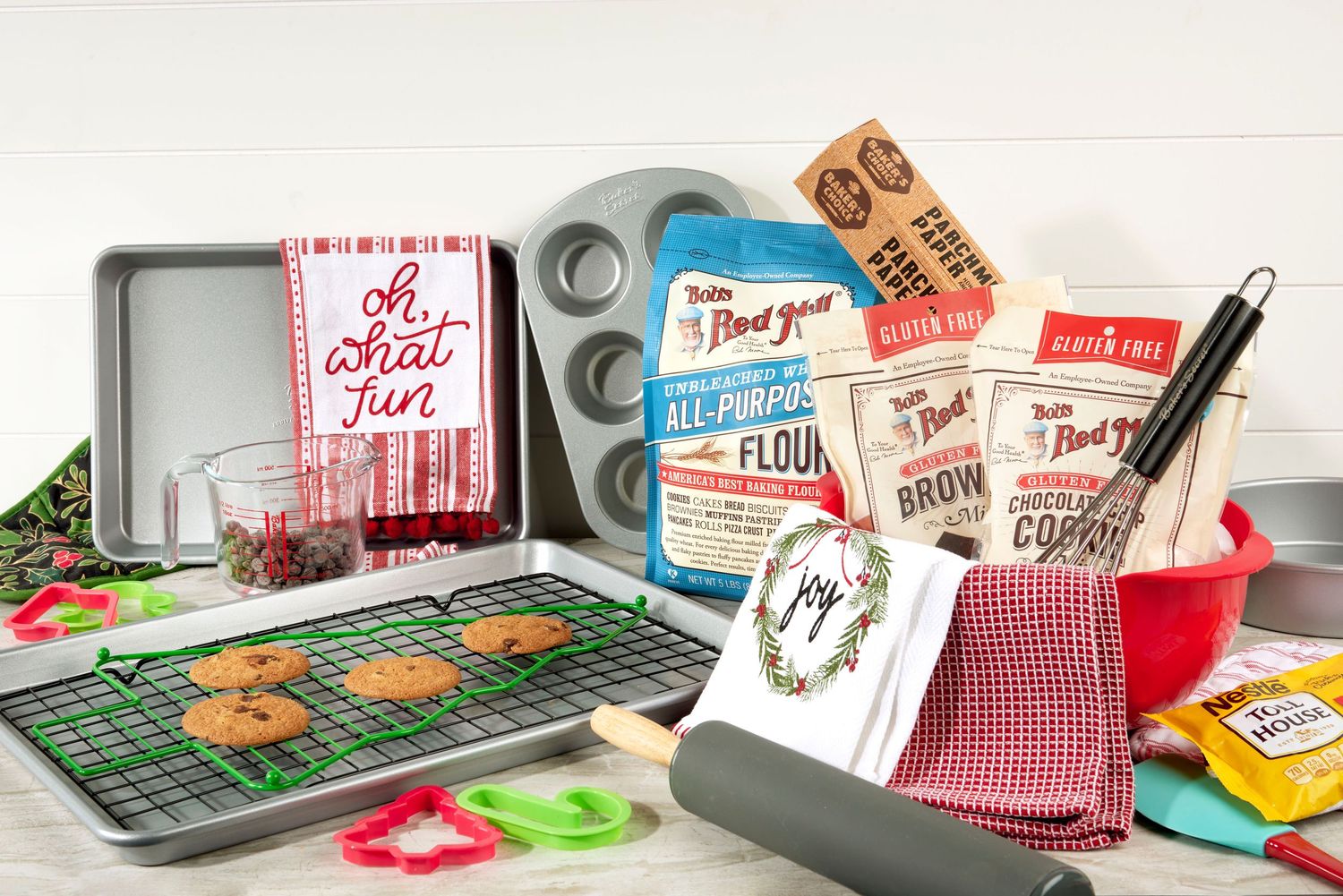 Holiday baking set with Bob's Red Mill flour, brownie mix, muffin tin, cooling rack, cookies, and festive kitchen towels.