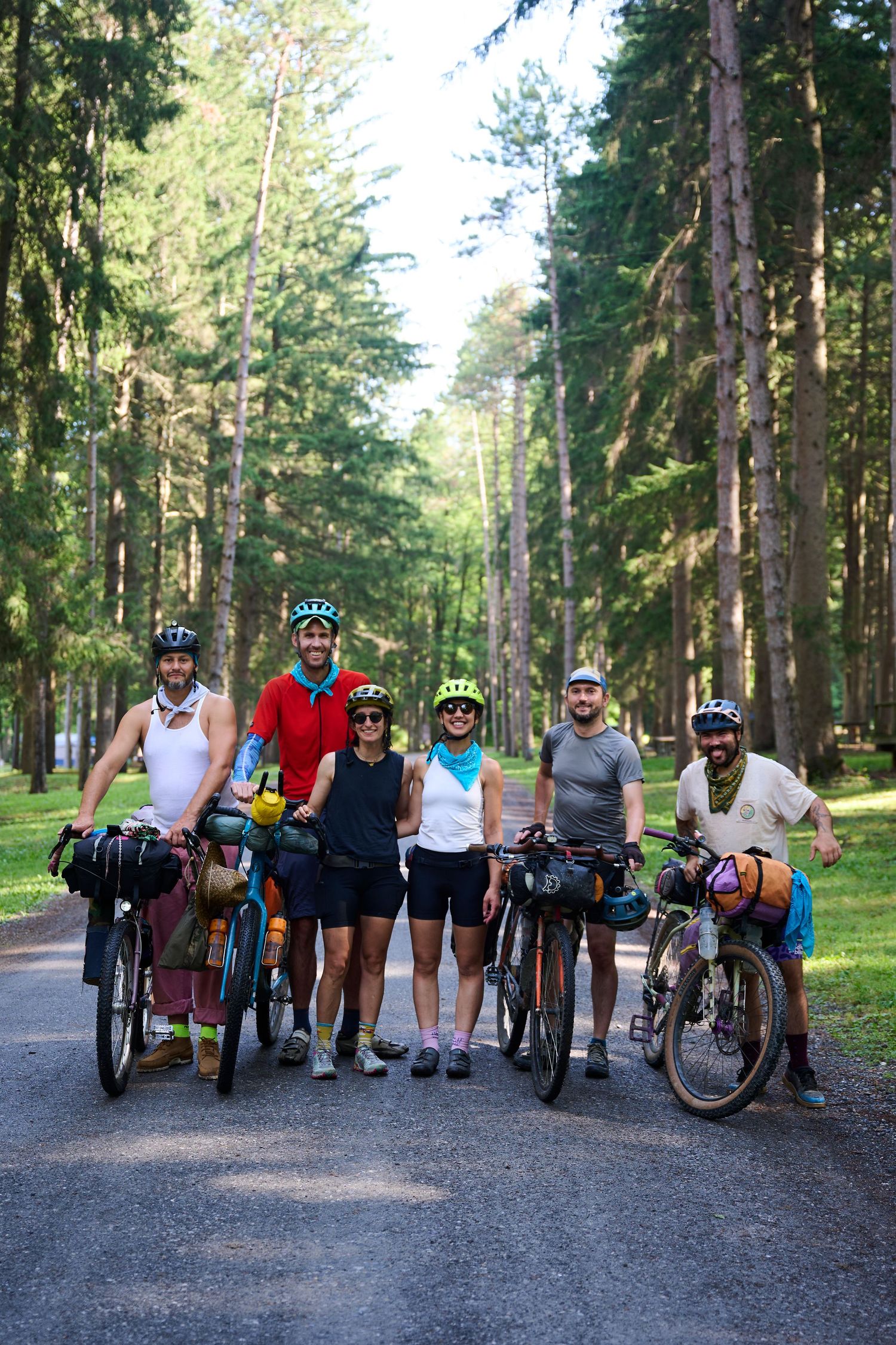 Group of cyclists with loaded bikes posing together on forest trail.