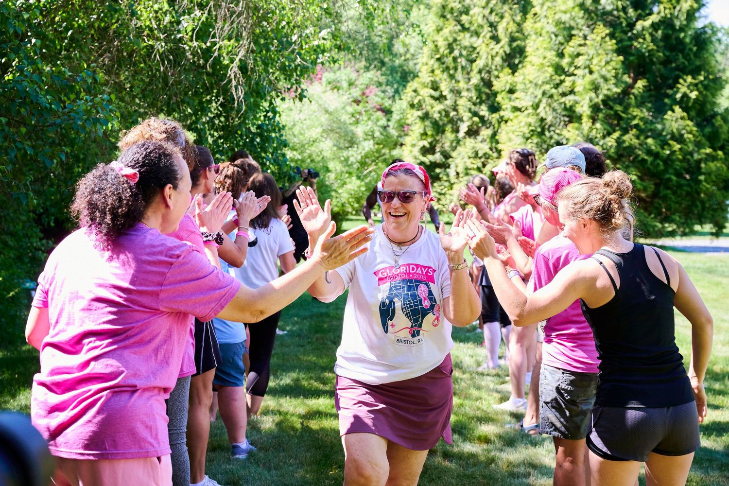 Women in pink shirts celebrate with high-fives during an outdoor charity run event on a sunny day.
