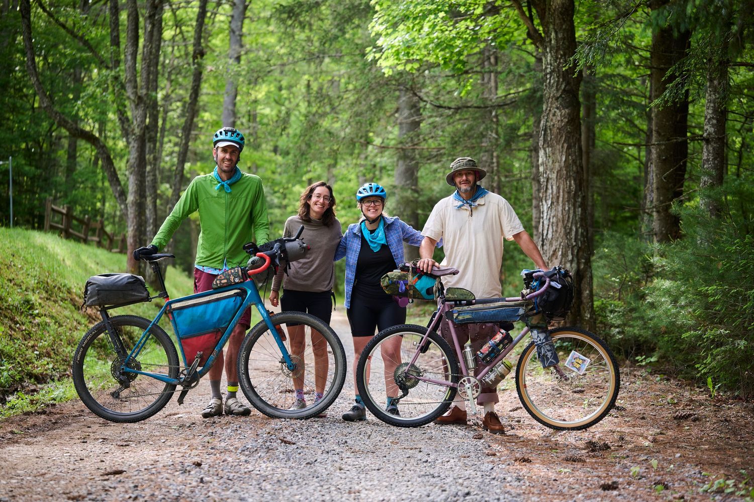 Four cyclists posing with bikepacking bikes on a forest gravel path surrounded by lush green trees.