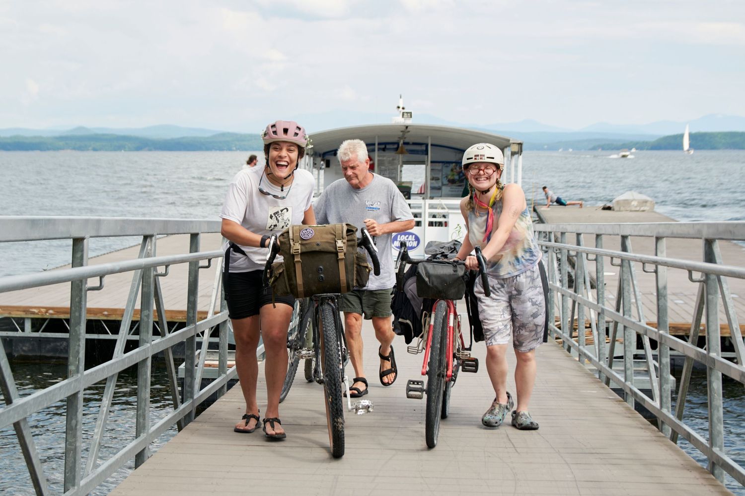Cyclists riding along a wooden pier by the waterfront on a sunny day.