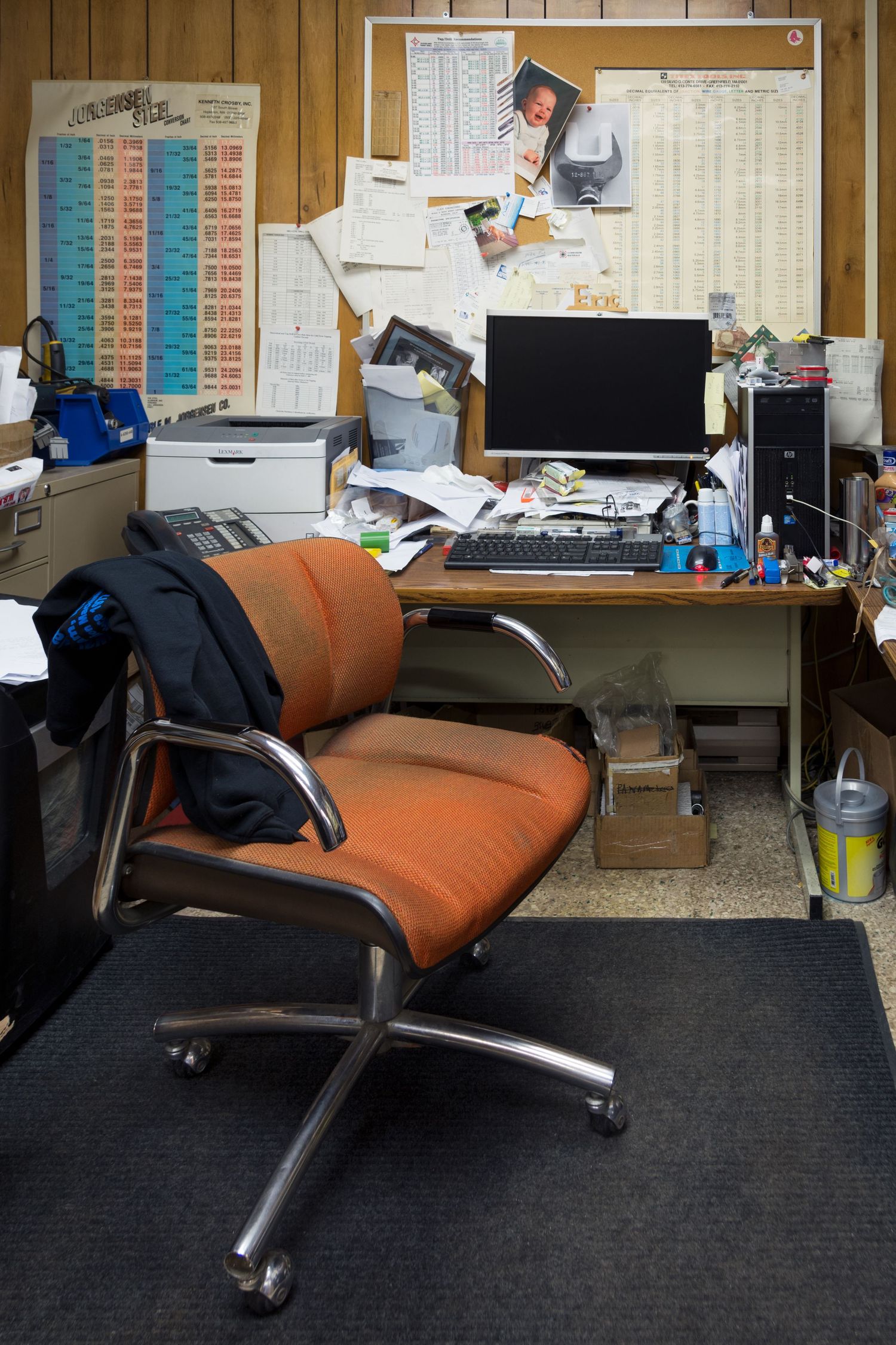 Modern office space with an orange reclining chair and wood paneled walls.