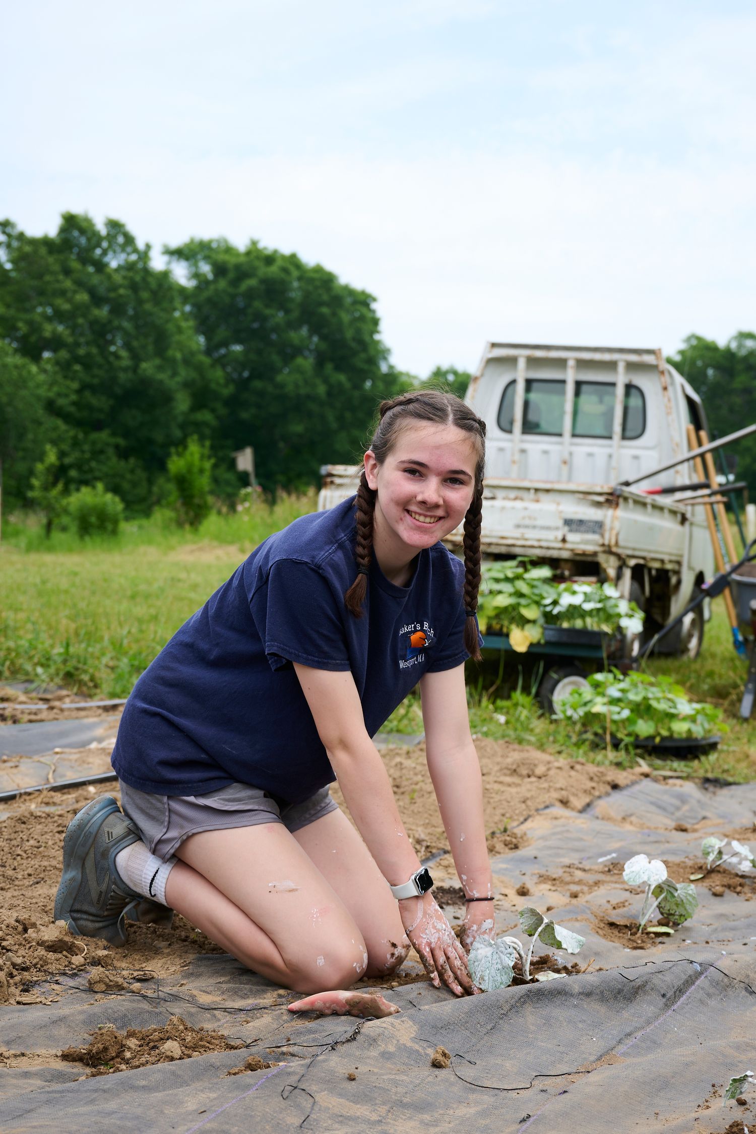 Young woman smiling while planting crops on a farm with black plastic mulch, wearing a blue polo shirt.