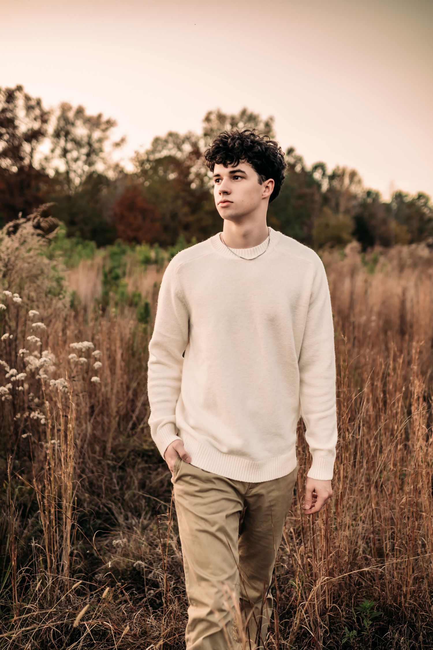 A teenager walks through a grassy field and looks out to his right.