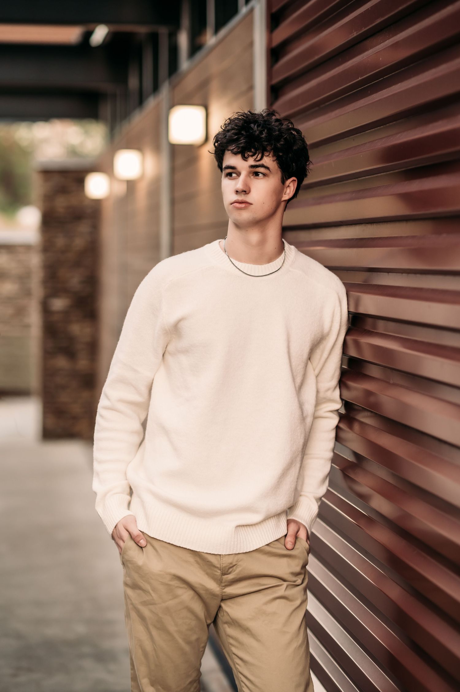 A senior teen leans against a red wall and looks out away from the wall.