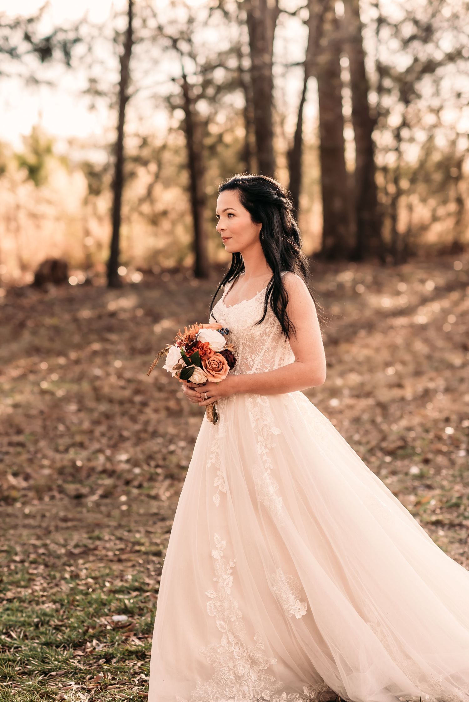 Bride walking down her grassy aisle while holding a bouquet of flowers with deep oranges and creams.