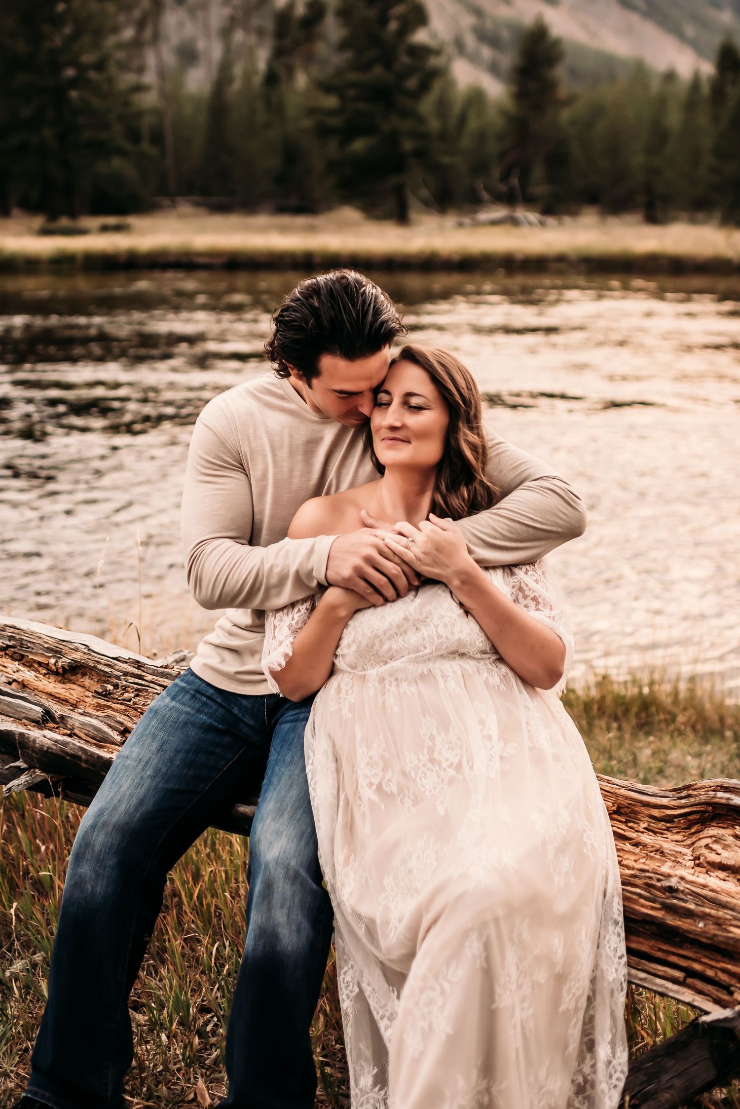 Couple snuggling on a log overlooking a lake in Yellowstone.