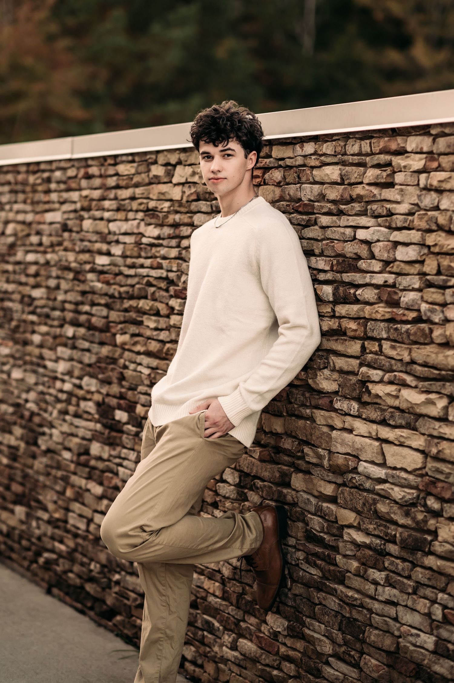 A senior boy leans against a stone wall and poses for his senior photo shoot in Charlotte, NC.