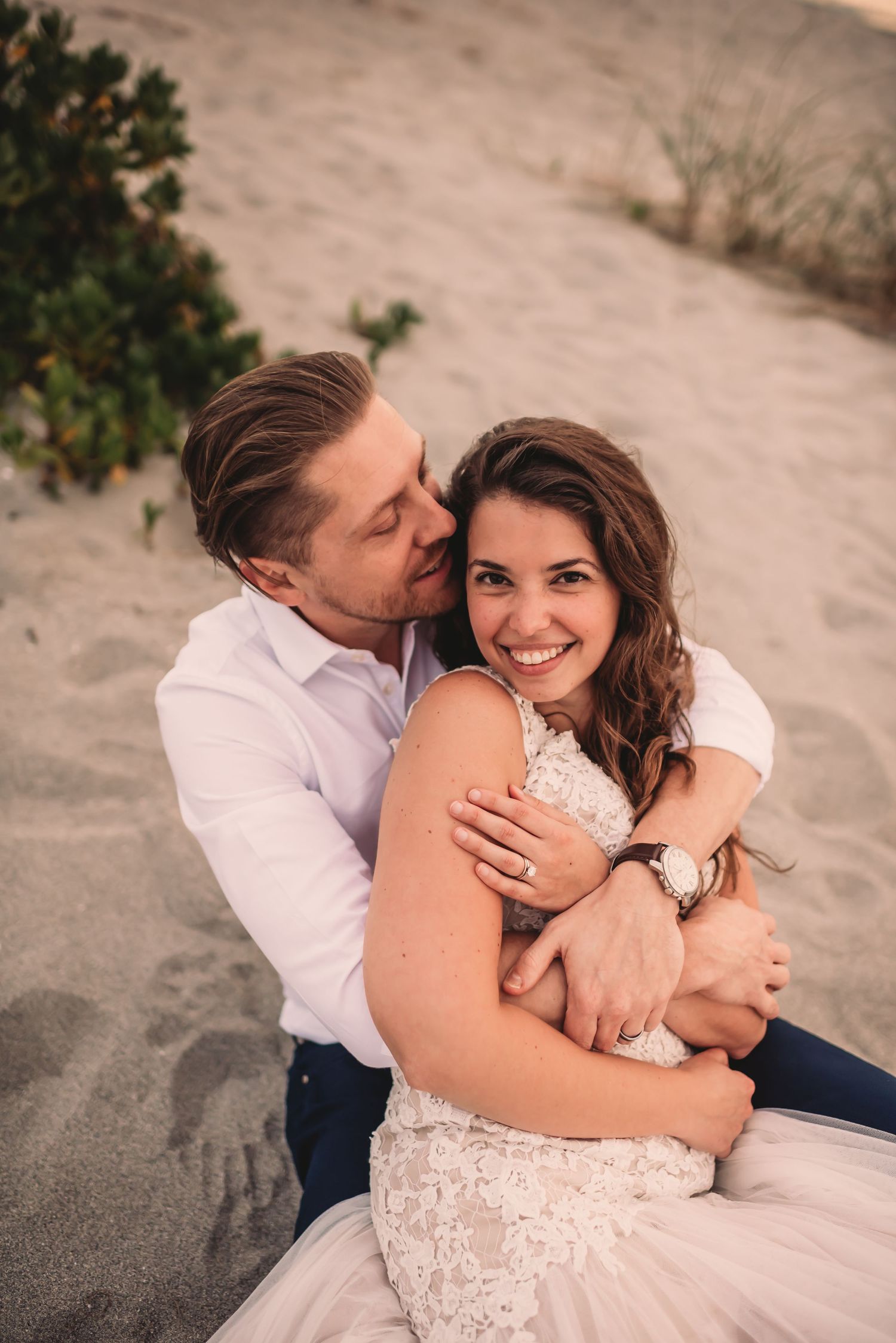 Newly married couple snuggles on the beach in the sand.