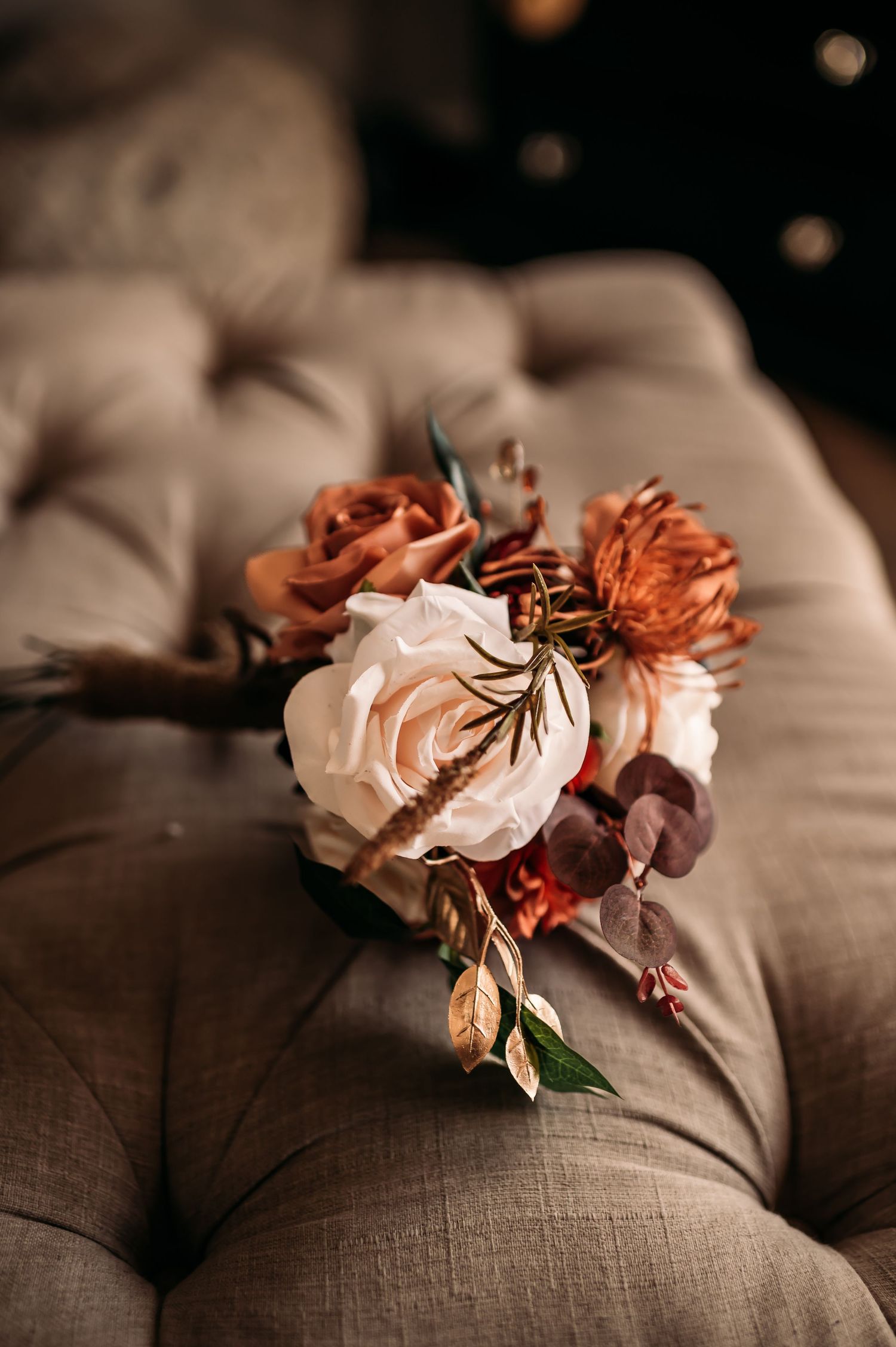 A bride's bouquet with burnt oranges, greens, and cream flowers.