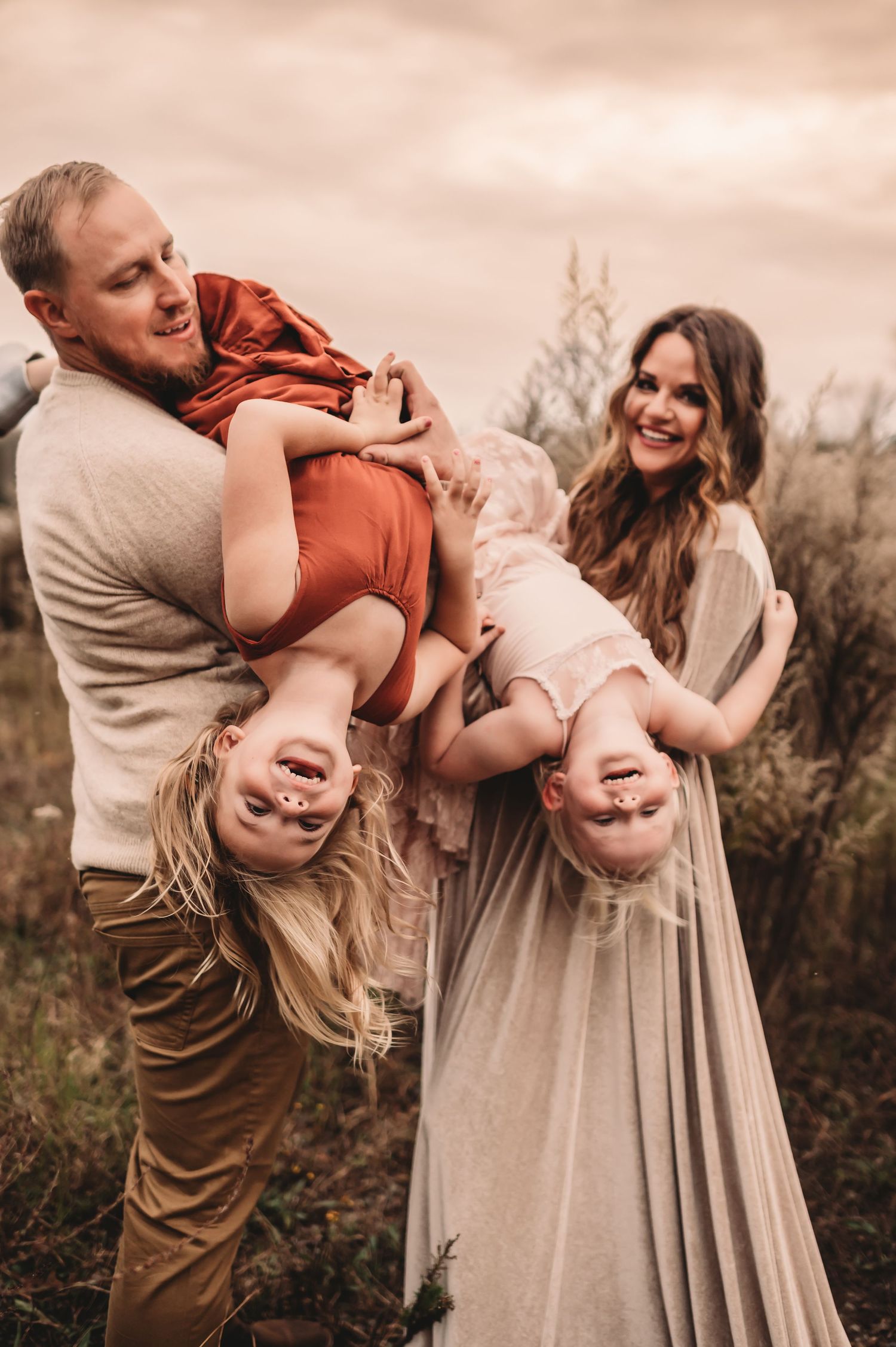 A man and woman holding their two daughters upside down while the girls laugh.