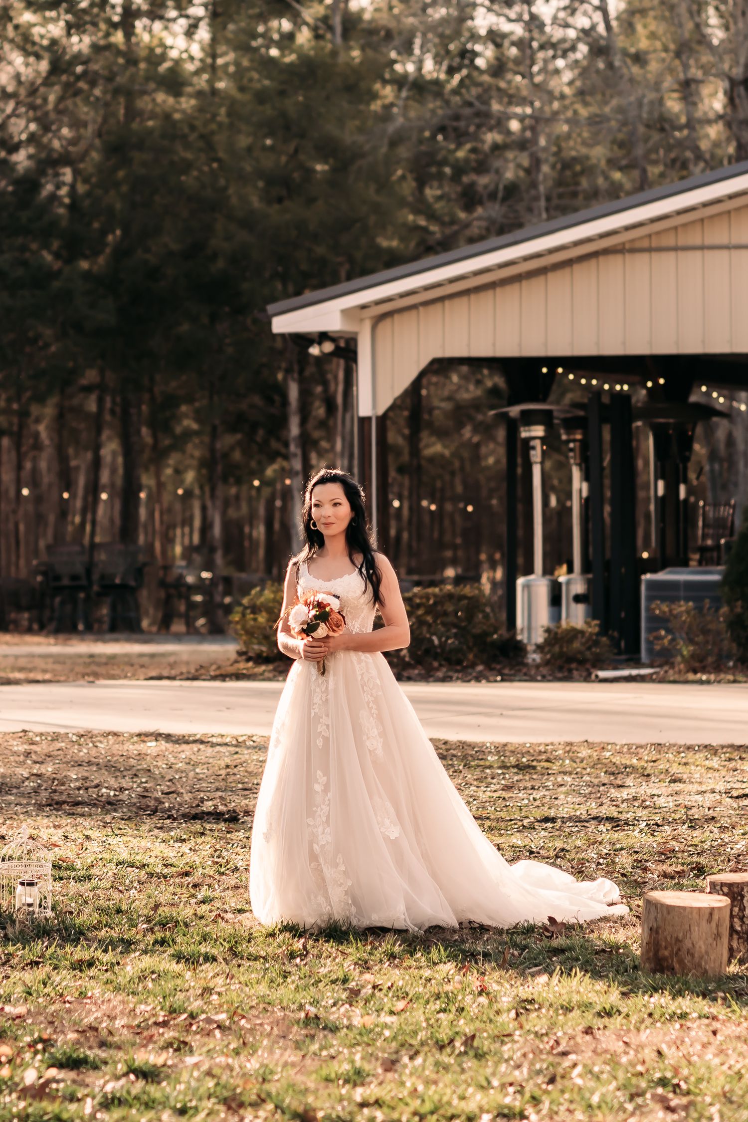 Bride walking down her grassy aisle while holding a bouquet of flowers with deep oranges and creams in front of a farm house.