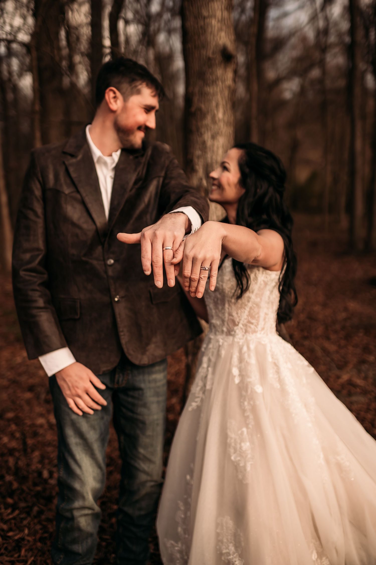 Newly married couple show off their rings by holding out their hands and smiling at one another.