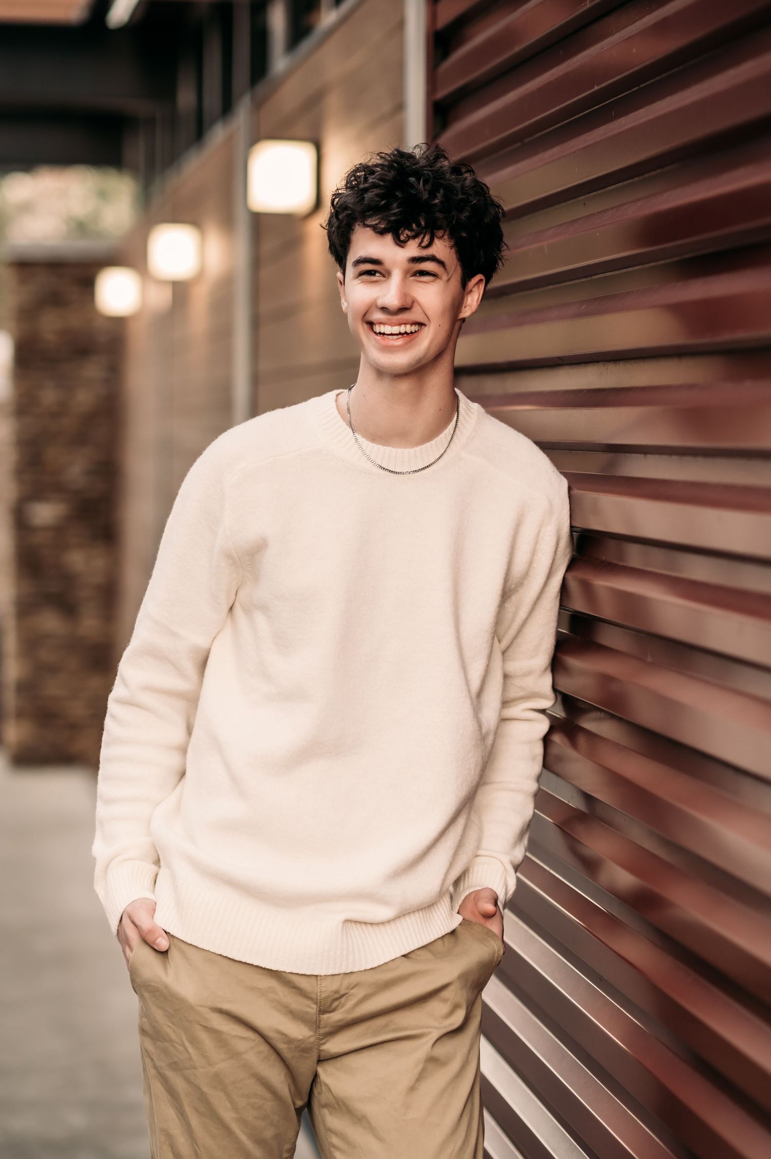 A teen leans against a red lined wall and laughs.