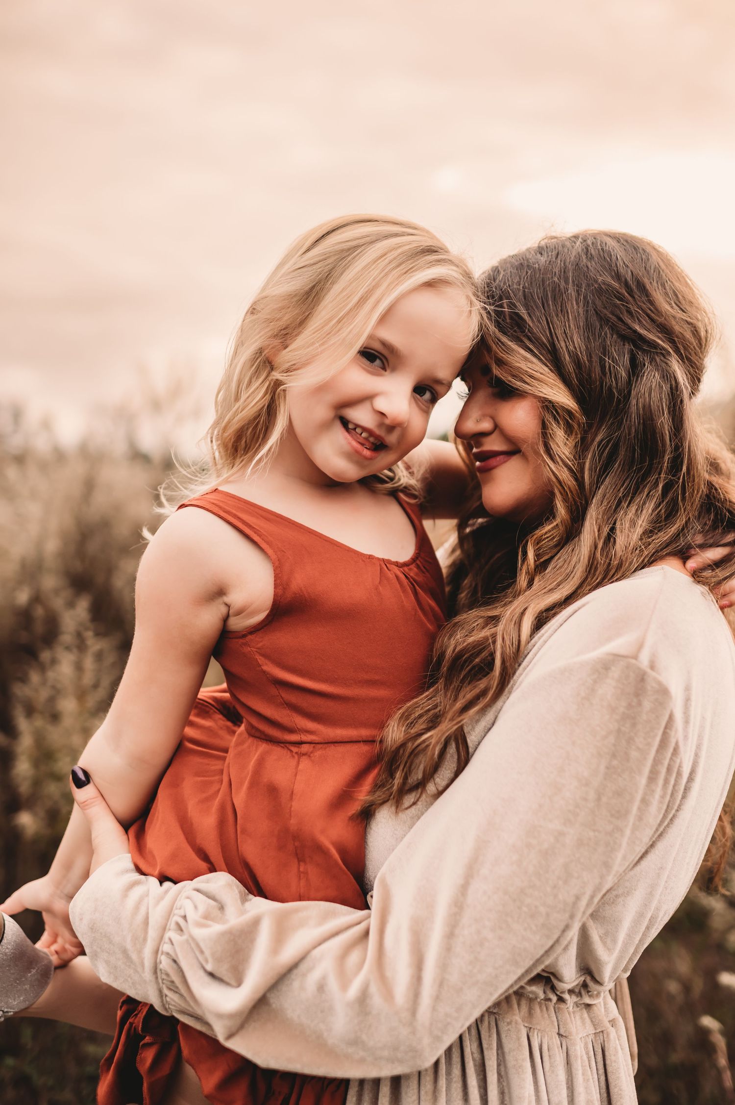 A mother snuggling close with her daughter while the little girl smiles at the camera.