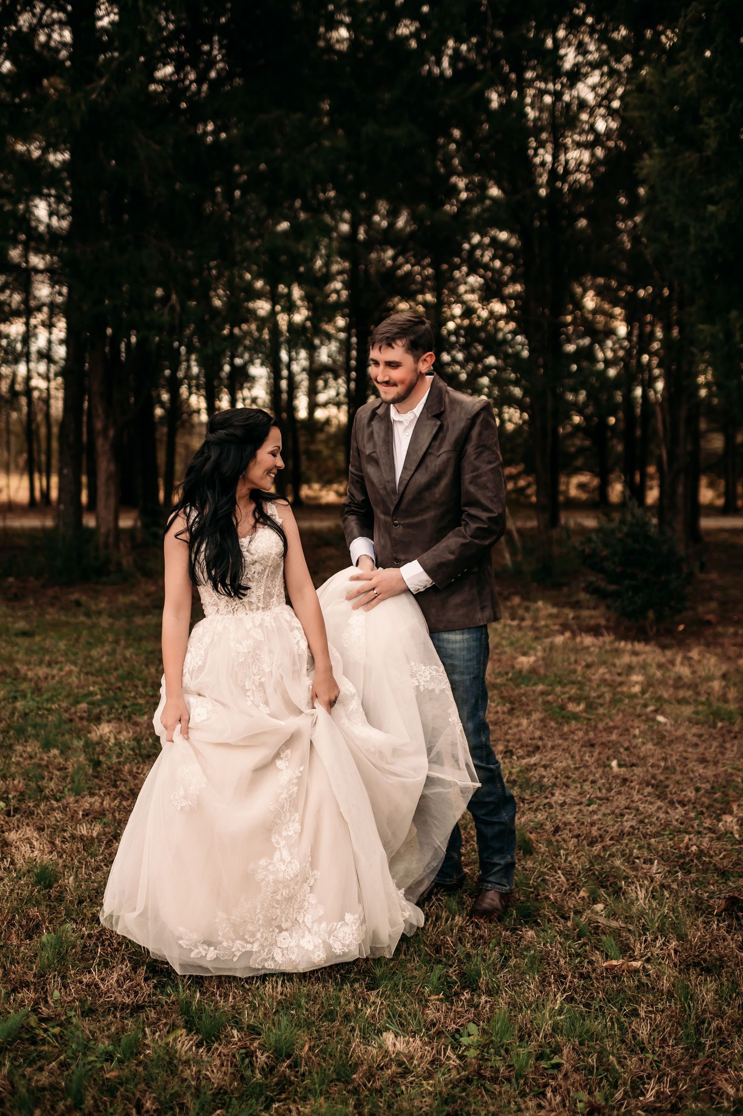 Groom is holding up bride's wedding dress train while they look at each other and smile.