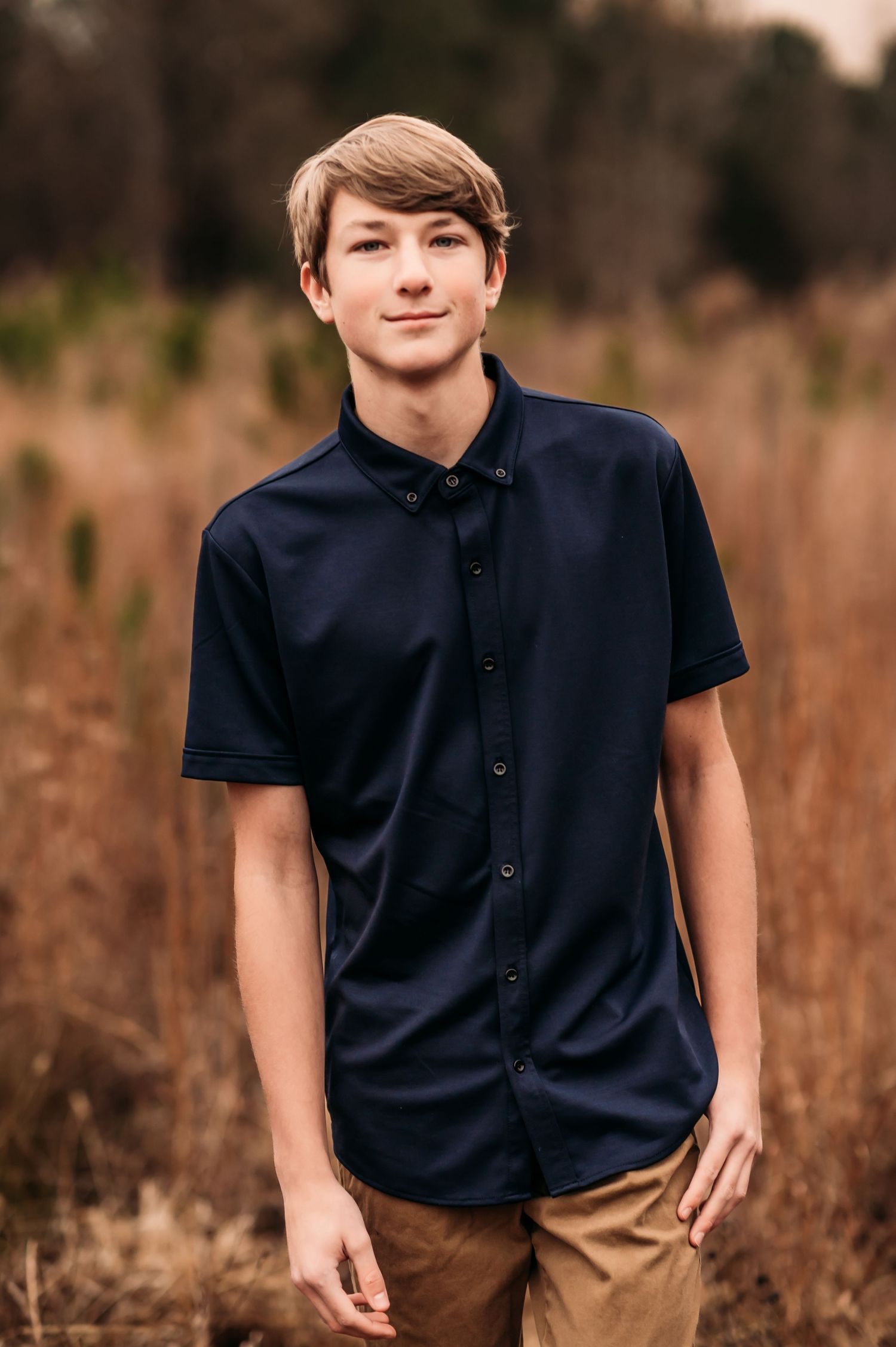 Teenage boy walking and looking through a grass field during sunset.