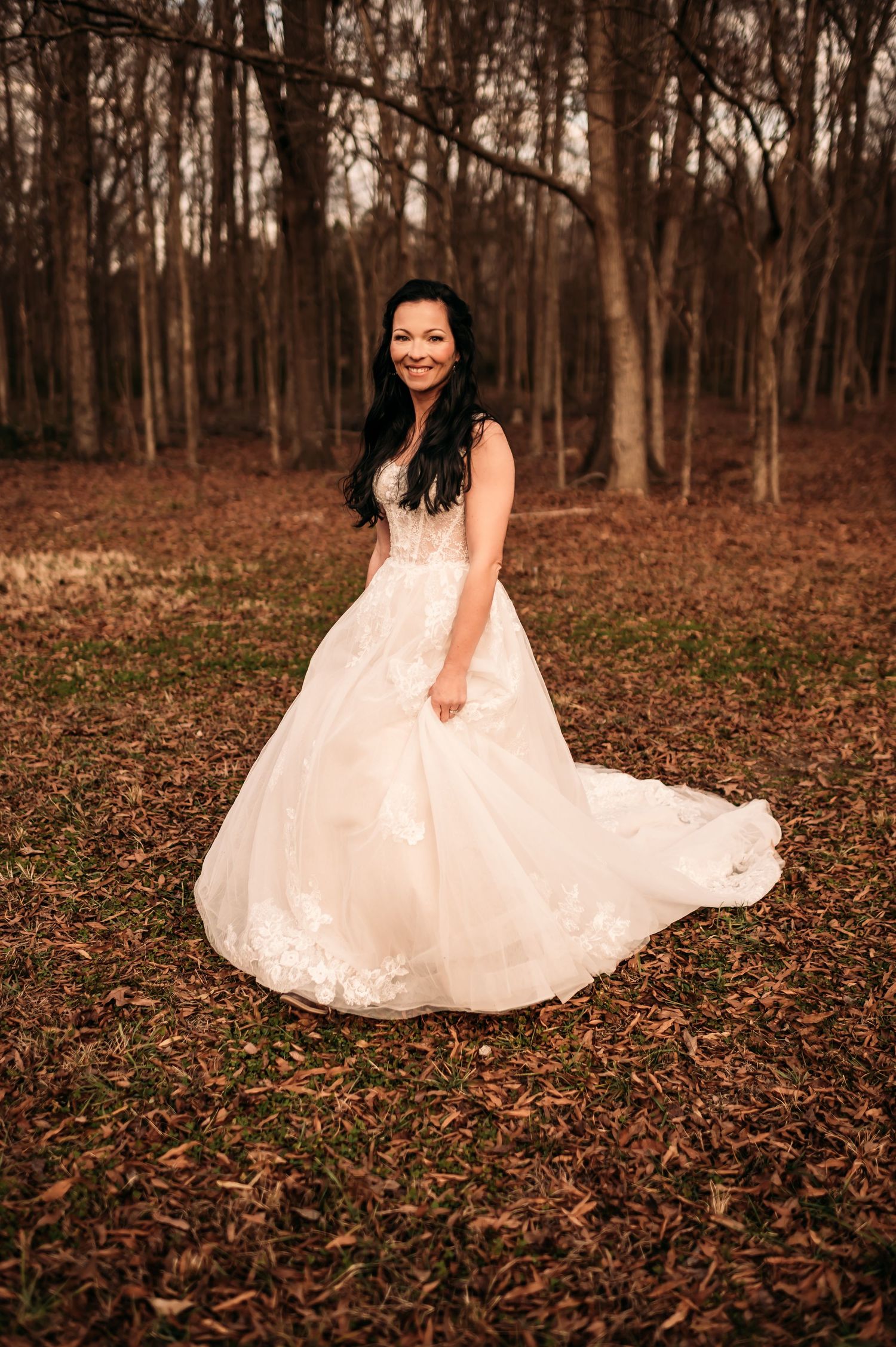 A bride looking at the camera and smiling while walking through fallen leaves.