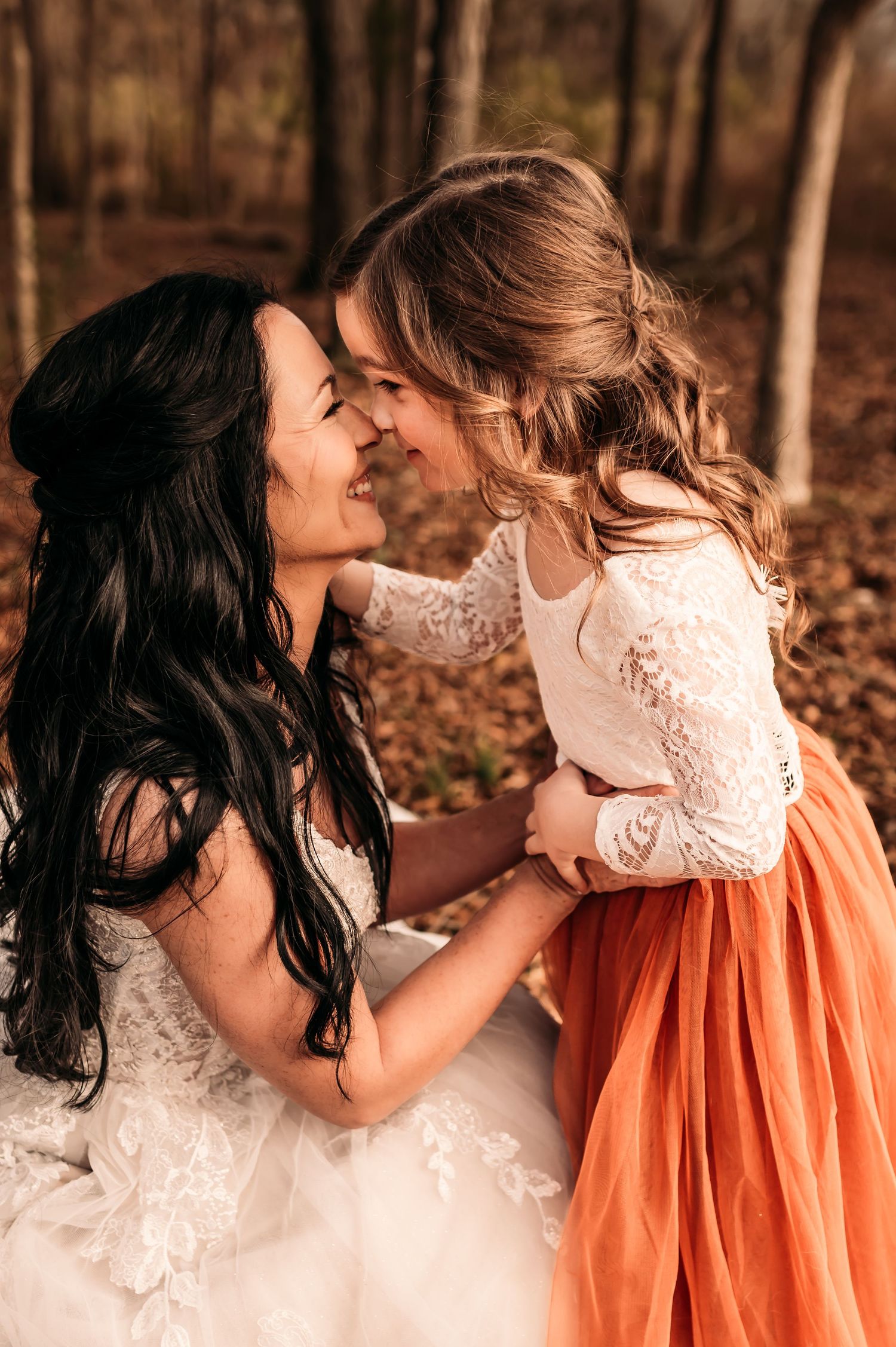 Mother and daughter rubbing noses and smiling while mother wears a wedding dress.