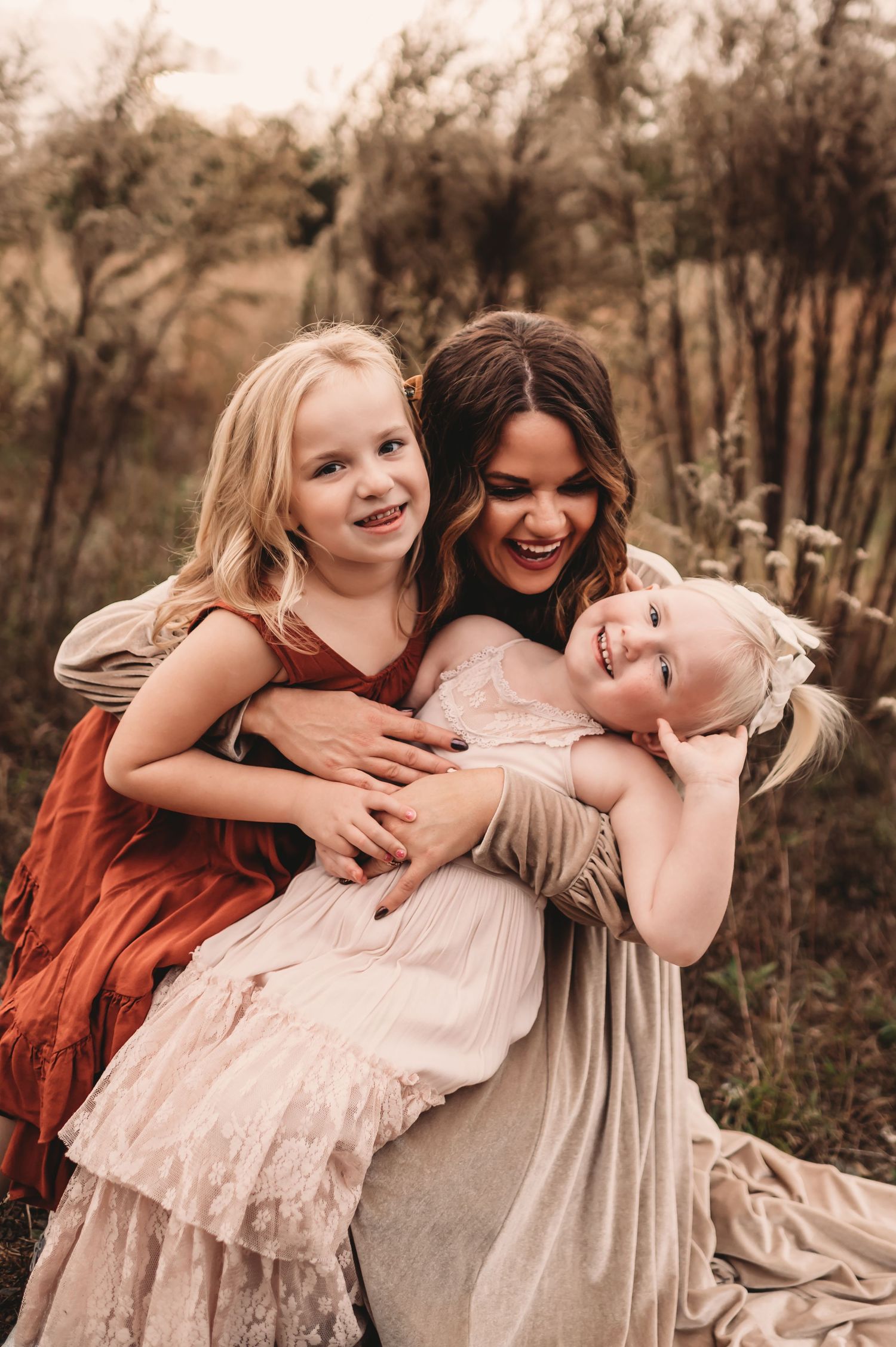 A mother hugging her laughing daughters in a field while Fallon Photography from Charlotte, North Carolina captures the moment.