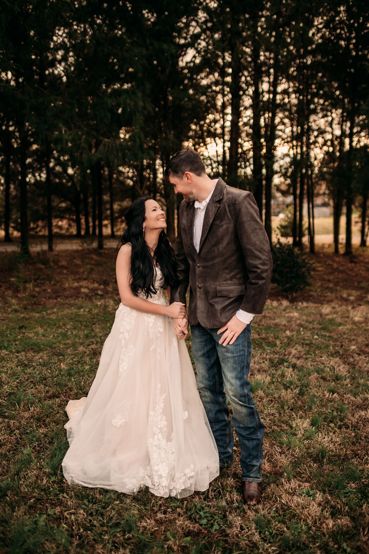 Bride looking up to groom and giggling with trees and sunset sky behind them.