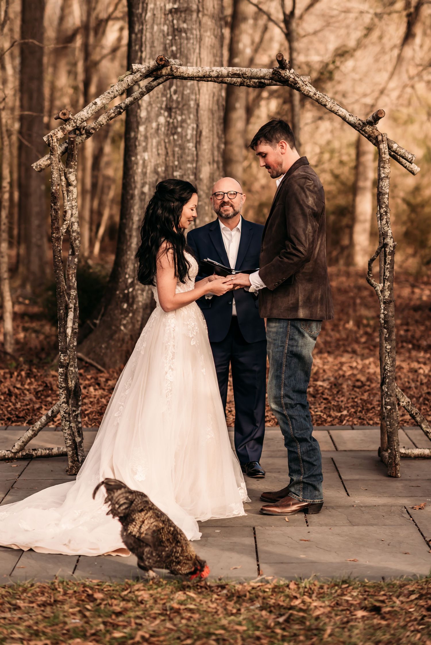 Bride and groom praying during ceremony with pastor behind them and a rooster in front of them.