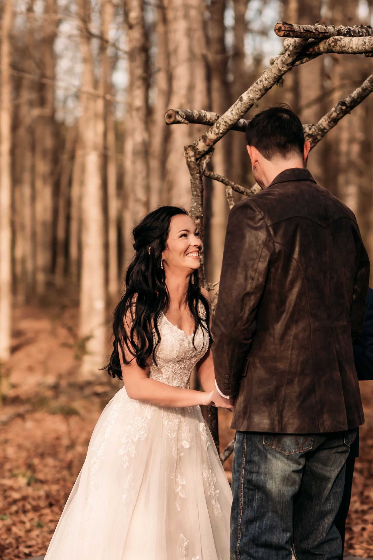 Bride laughing while saying vows to groom surrounded by trees.